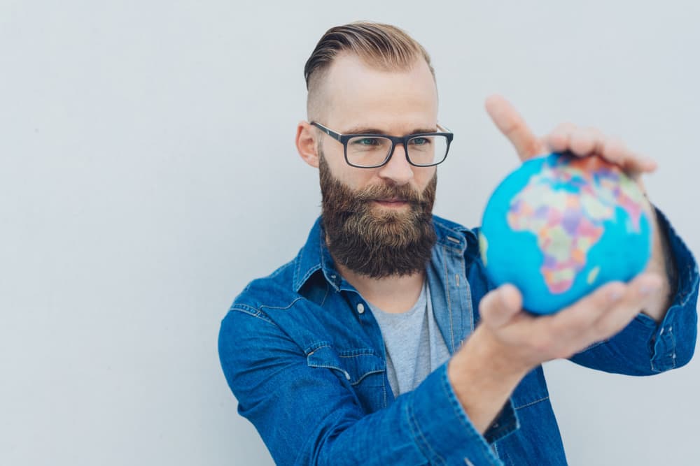 A man holding up a small globe and pointing at it