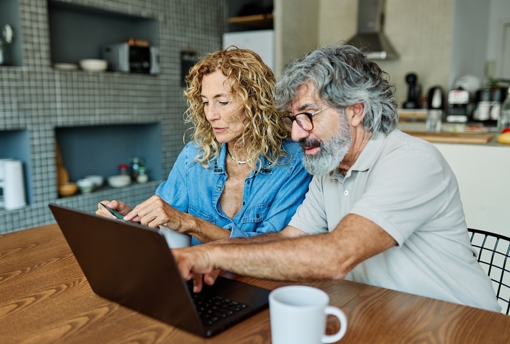 A couple at their kitchen table looking at a laptop together