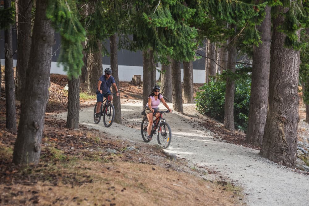 Elderly couple bikes down path through trees, Hamilton