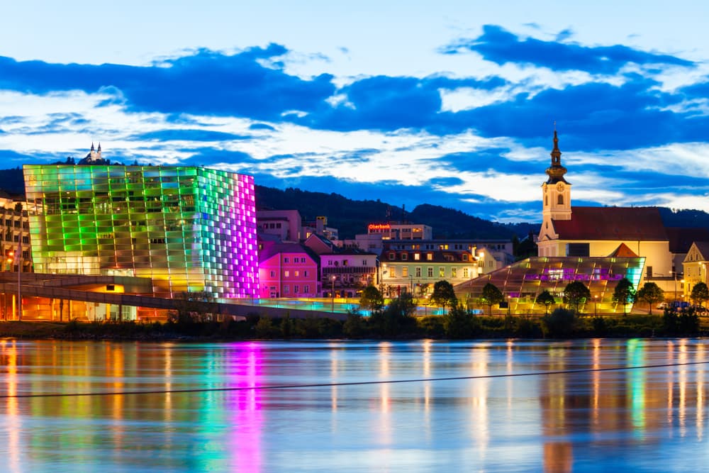 City buildings lit up at twilight by the river, Linz