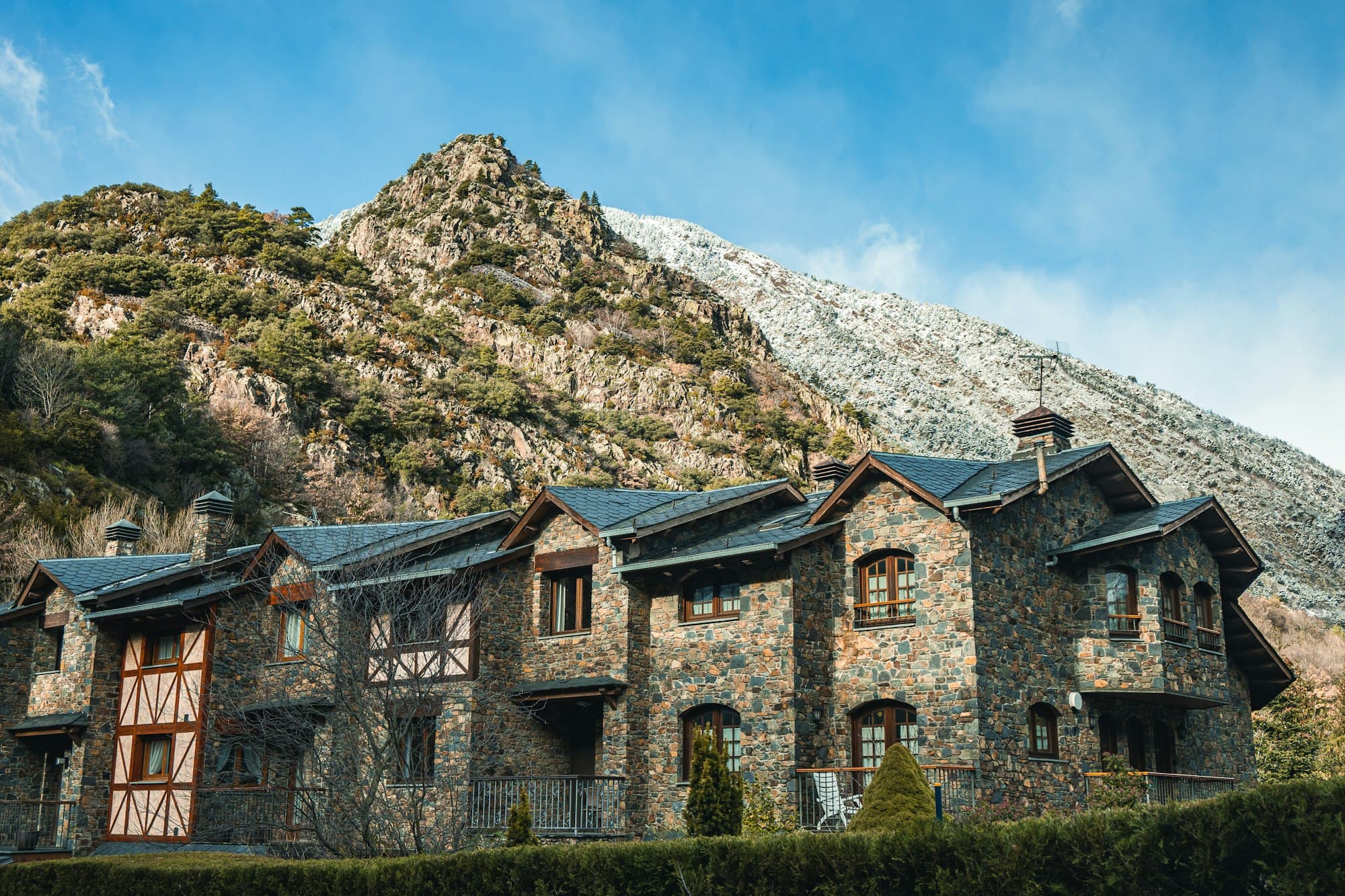 Stone houses with slate roofs below a rocky, snow-dusted mountain in Andorra