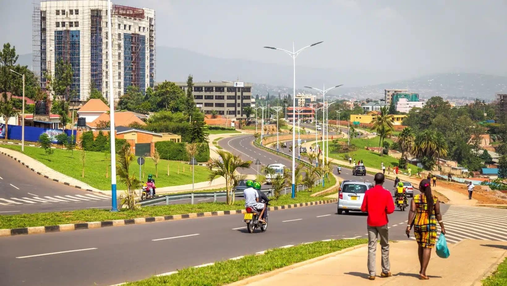 A wide landscaped boulevard in Kigali with pedestrians and motorbikes
