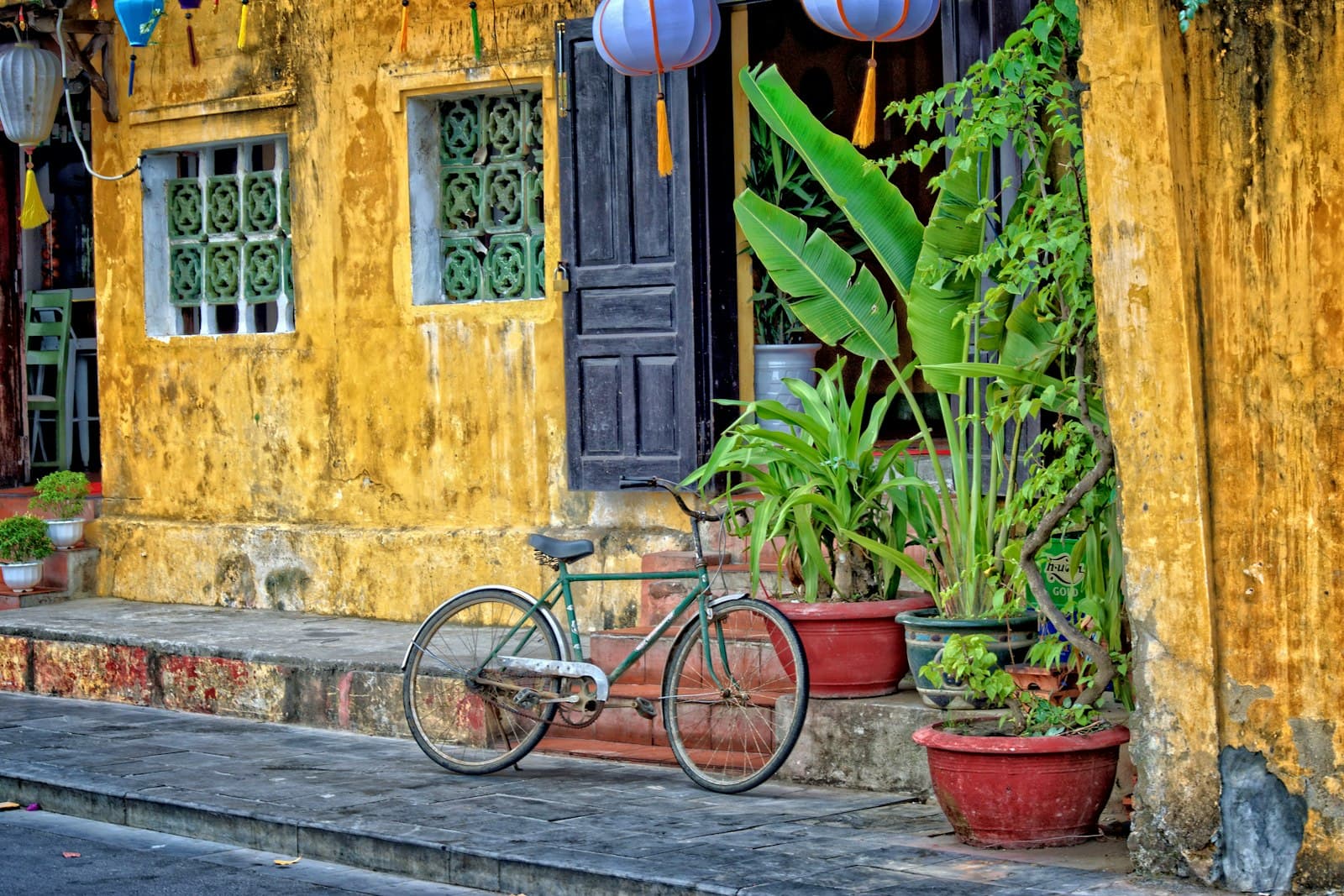 A green bicycle parked outside a yellow house with lanterns in Hoi An's old town