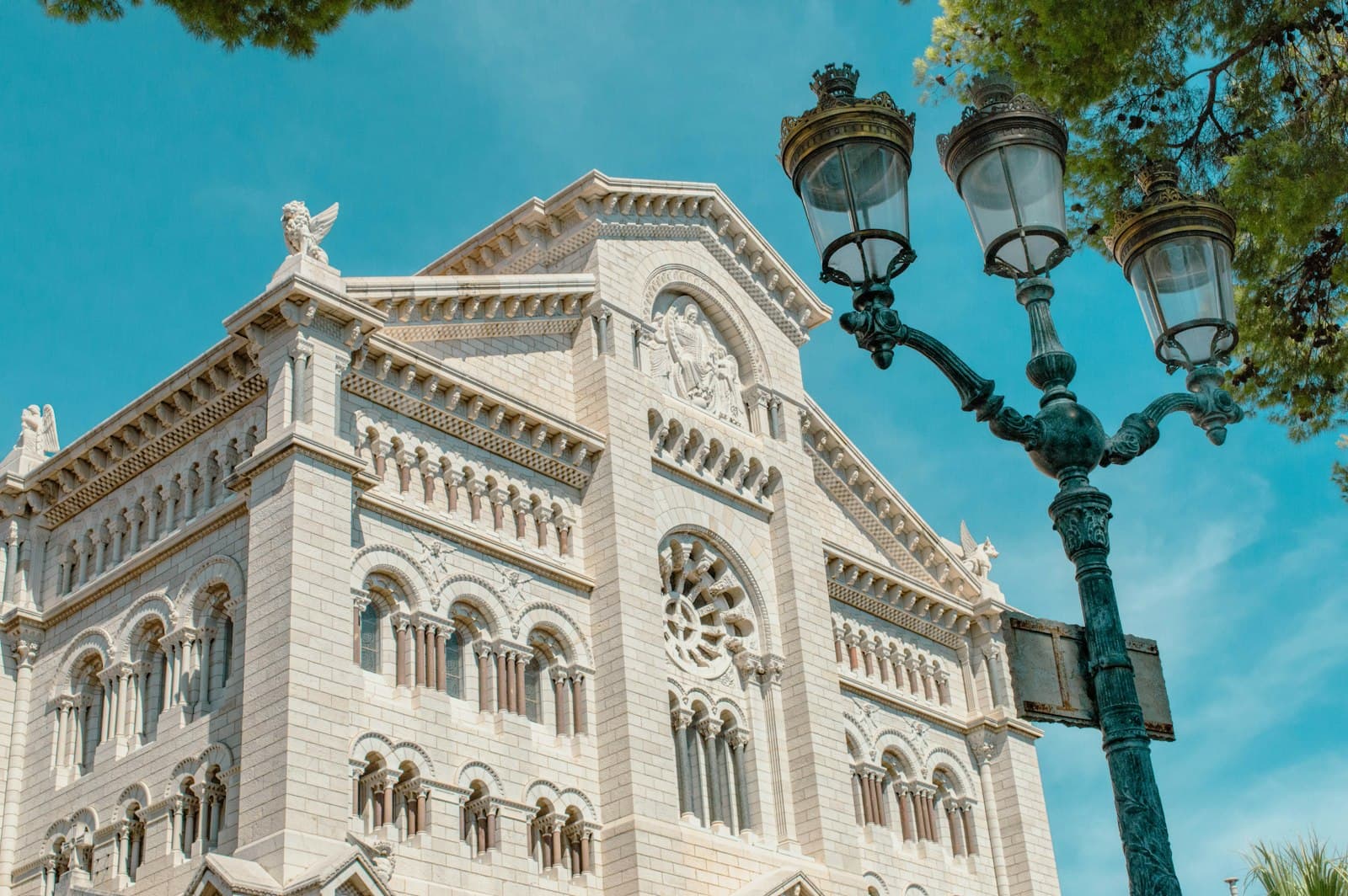 The white stone facade of Monaco Cathedral beside an ornate street lamp