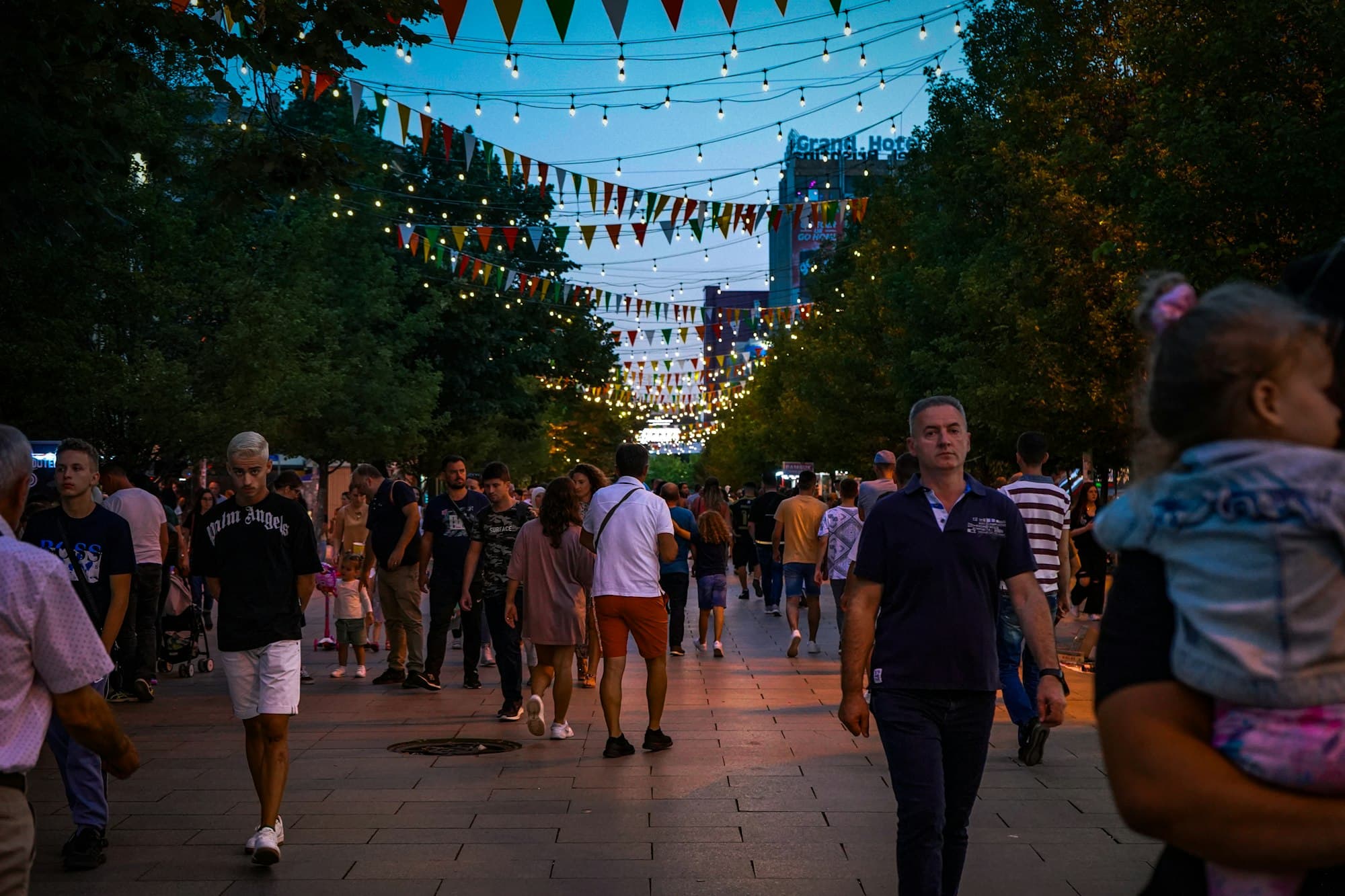 Evening crowd walking under string lights on Mother Teresa Boulevard in Pristina