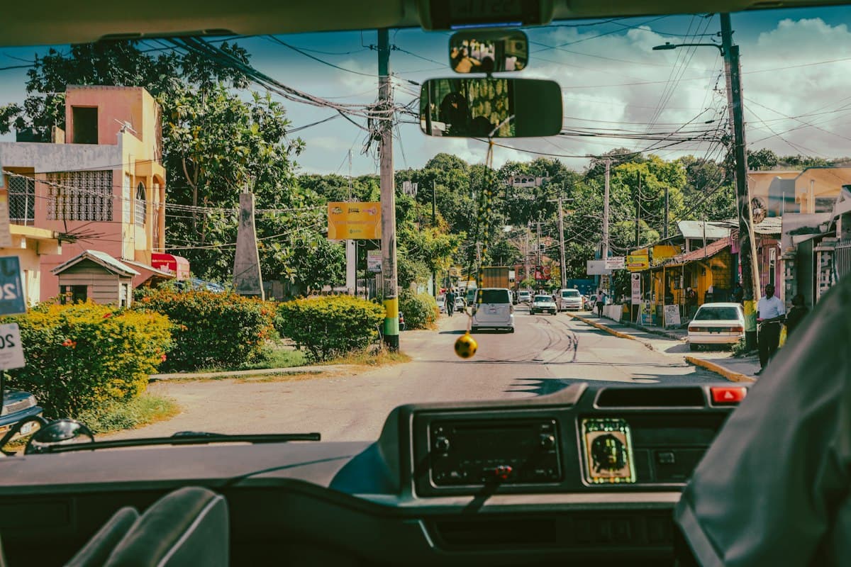 A tree-lined Jamaican street seen through the windshield of a local bus