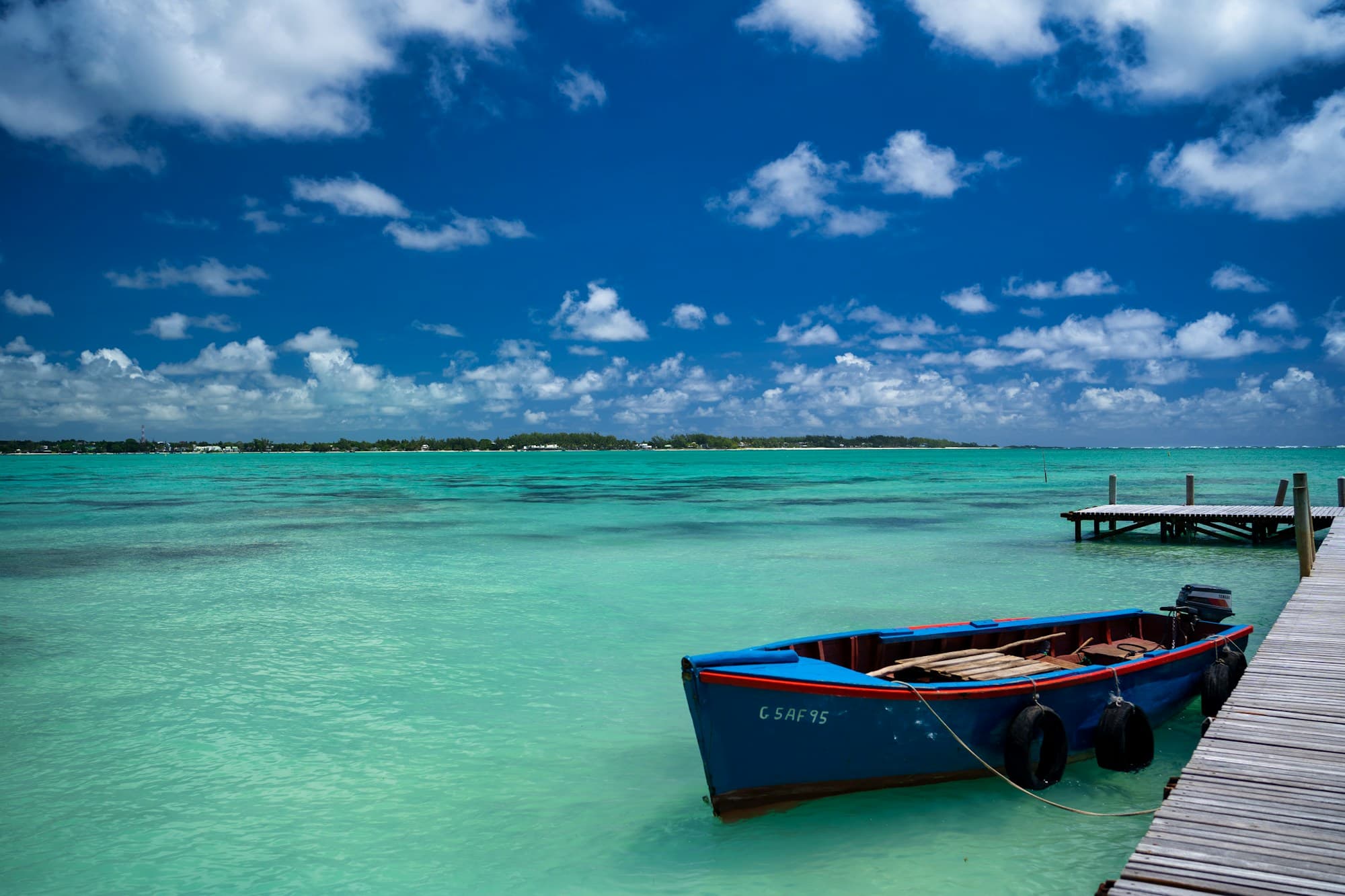 A blue wooden fishing boat tied to a jetty over turquoise lagoon water in Mauritius