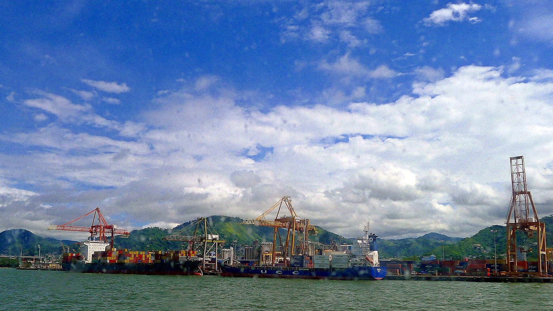 Container ships and cranes at the Point Lisas port on Trinidad's west coast, with green hills behind