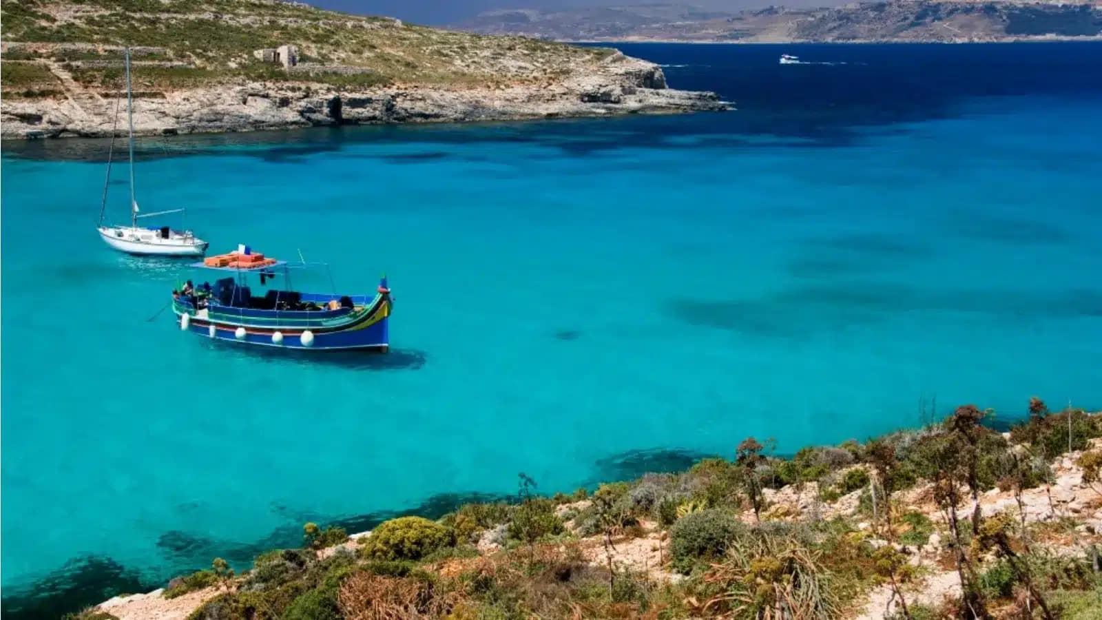 A traditional Maltese luzzu boat anchored in turquoise water off Comino