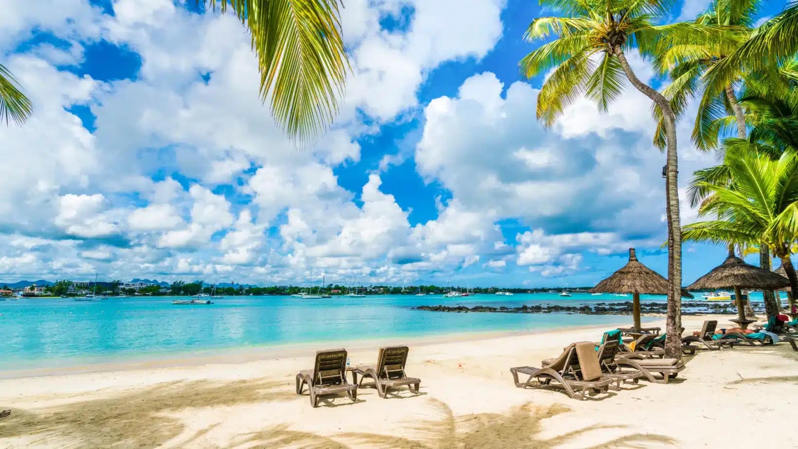 Palm trees and beach loungers on white sand facing the turquoise bay at Grand Baie, Mauritius