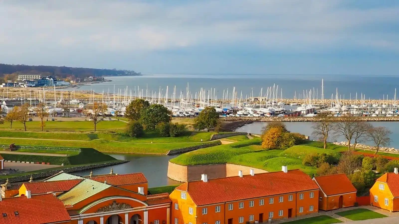 Orange-roofed buildings beside a harbor full of sailboats on the Danish coast