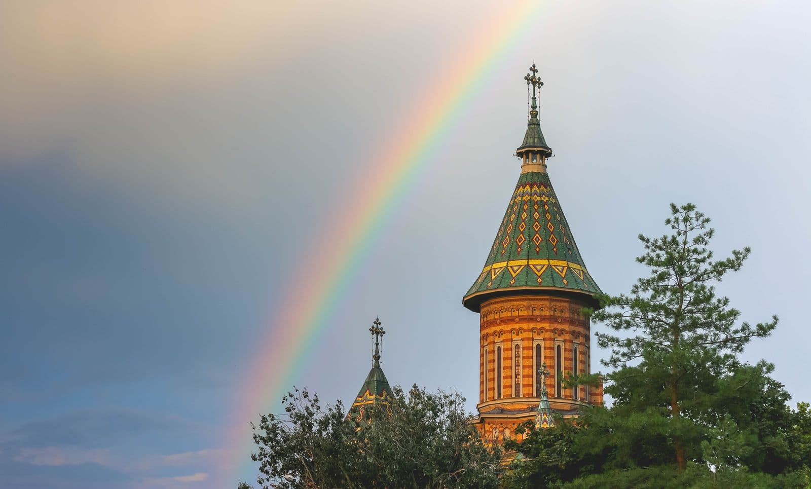 Green and gold tiled tower of Timișoara's Orthodox Cathedral under a rainbow