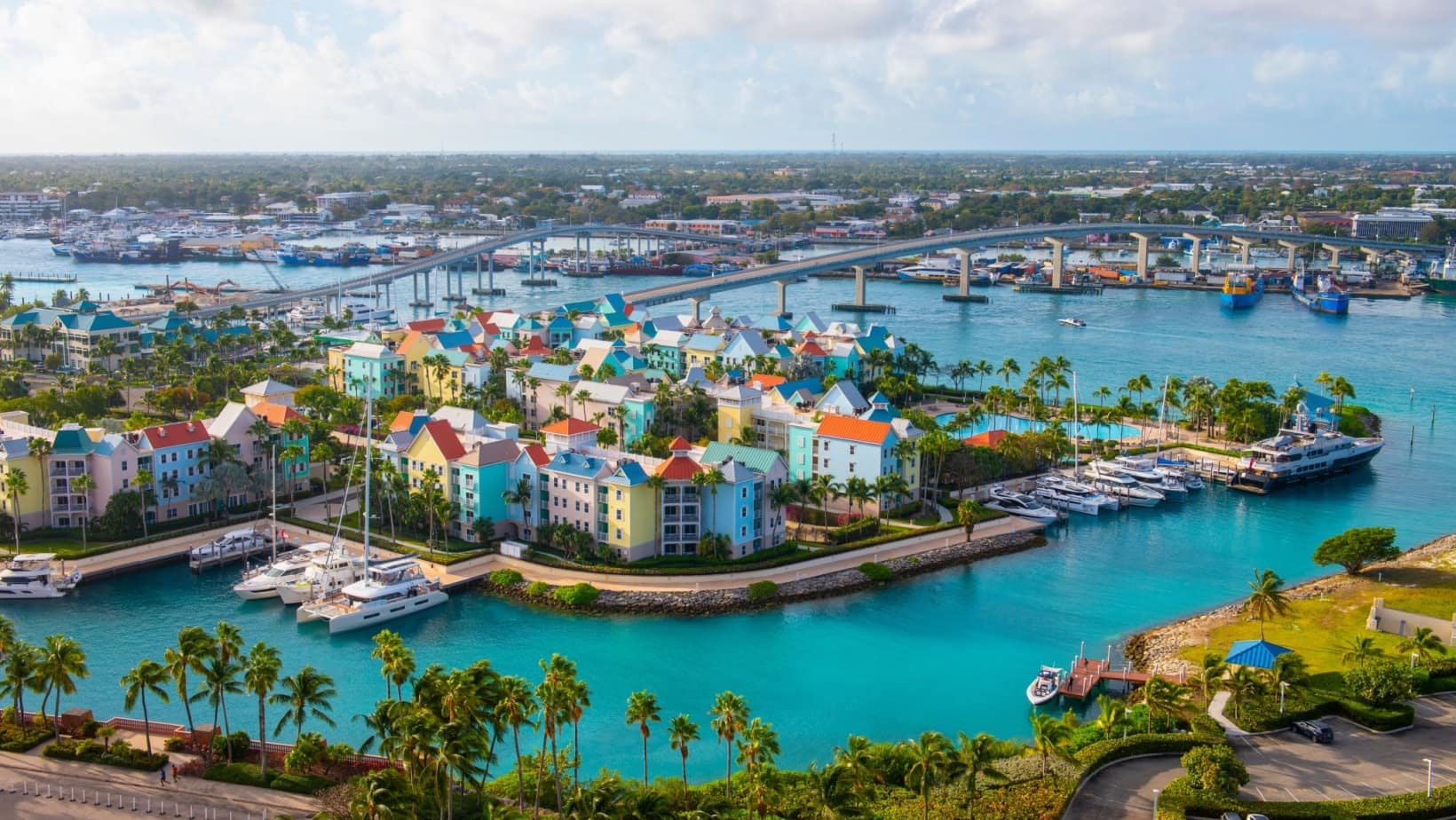 Aerial view of pastel homes and boat slips along the water in Nassau, with the harbor bridges behind