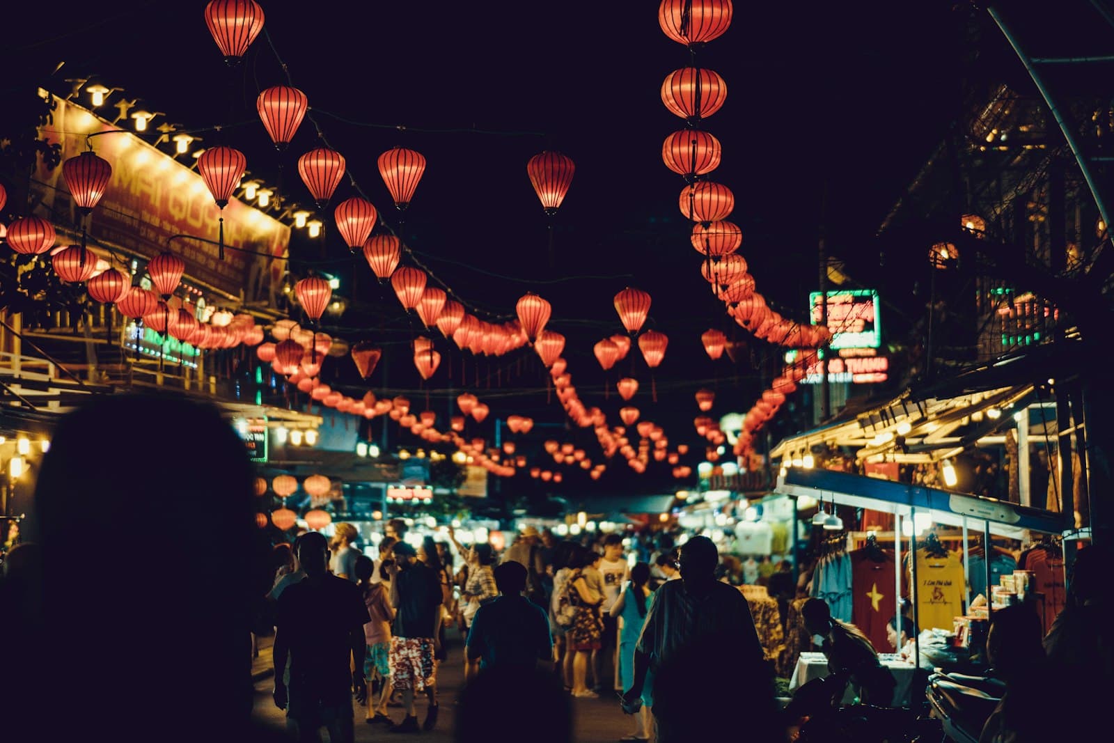 Red silk lanterns strung above a busy night market street in Vietnam