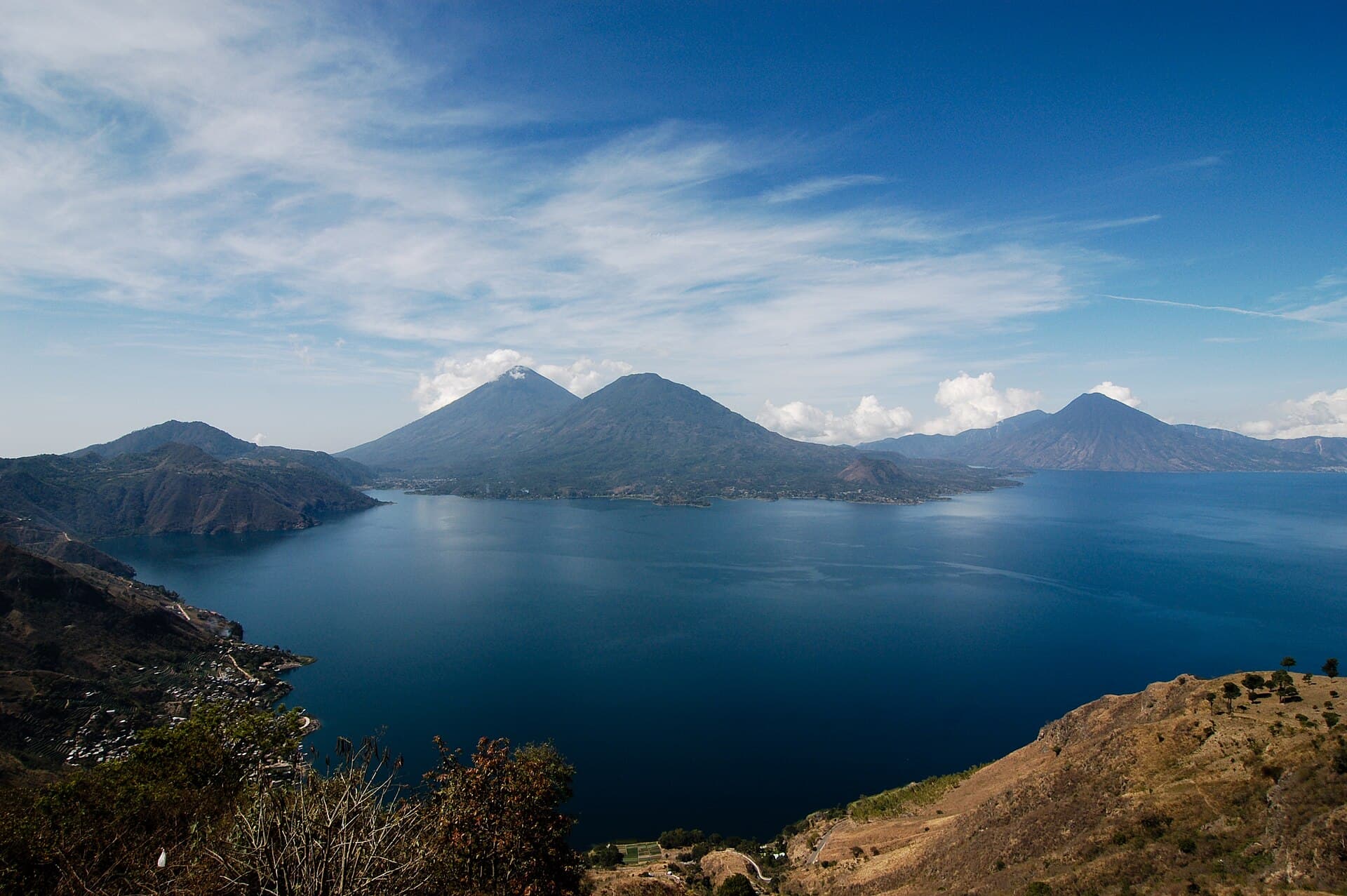 Lake Atitlán seen from a hillside, with three volcanoes across the water under a blue sky