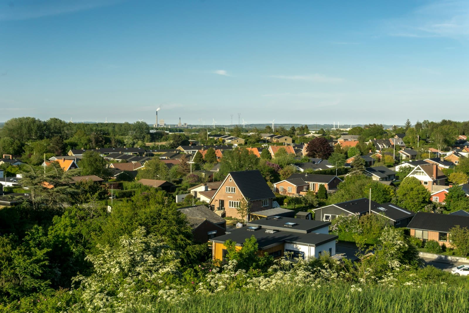 Brick family homes and gardens in a Danish neighborhood with wind turbines on the horizon