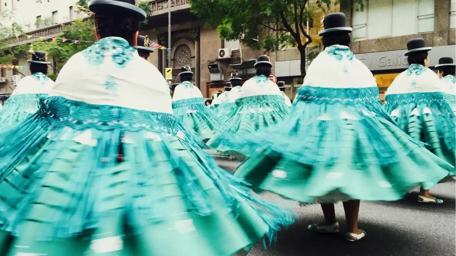 Cholitas in bowler hats and swirling turquoise skirts dancing in a Bolivian street parade