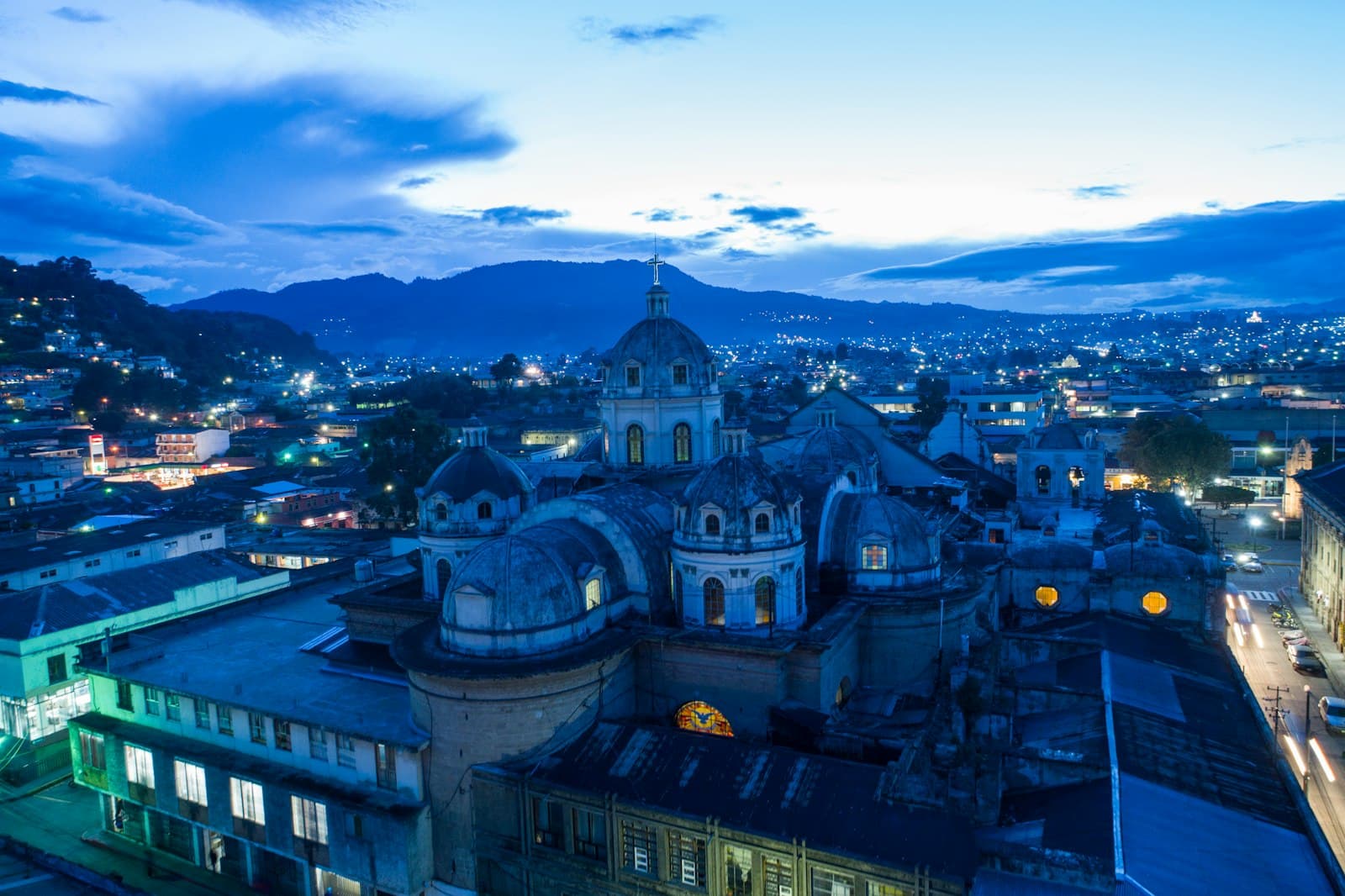 The domed cathedral of Quetzaltenango at dusk with city lights and mountains behind