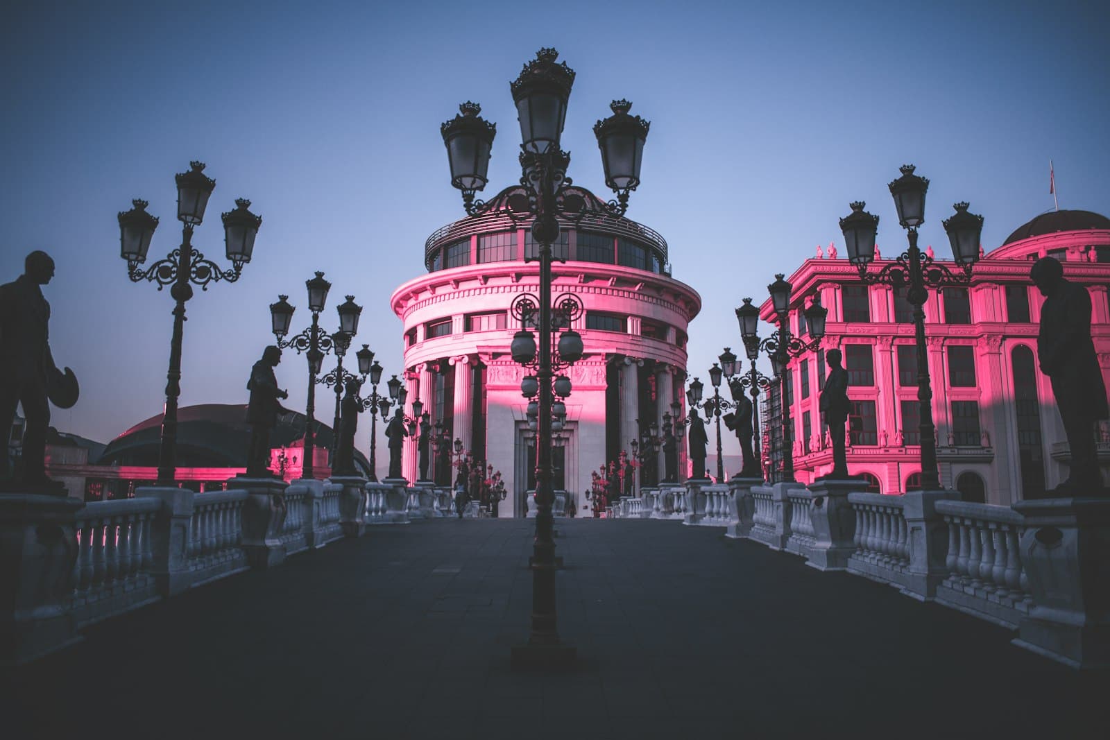 Ornate lampposts and statues on a pedestrian bridge in central Skopje at dusk