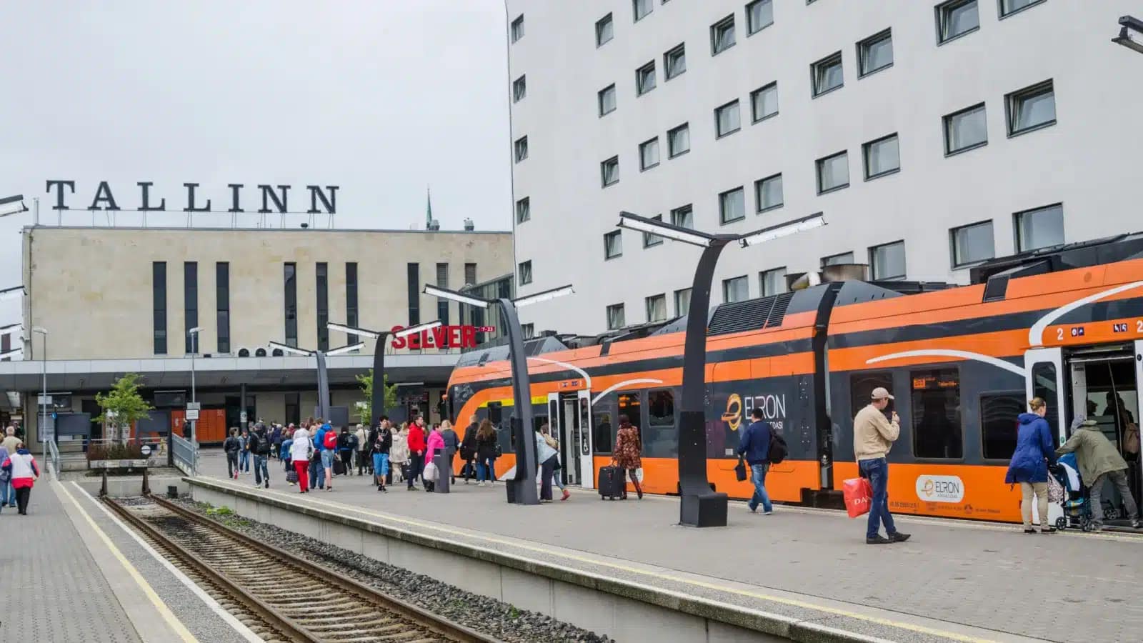Commuters on the platform beside an orange regional train at Tallinn's main station