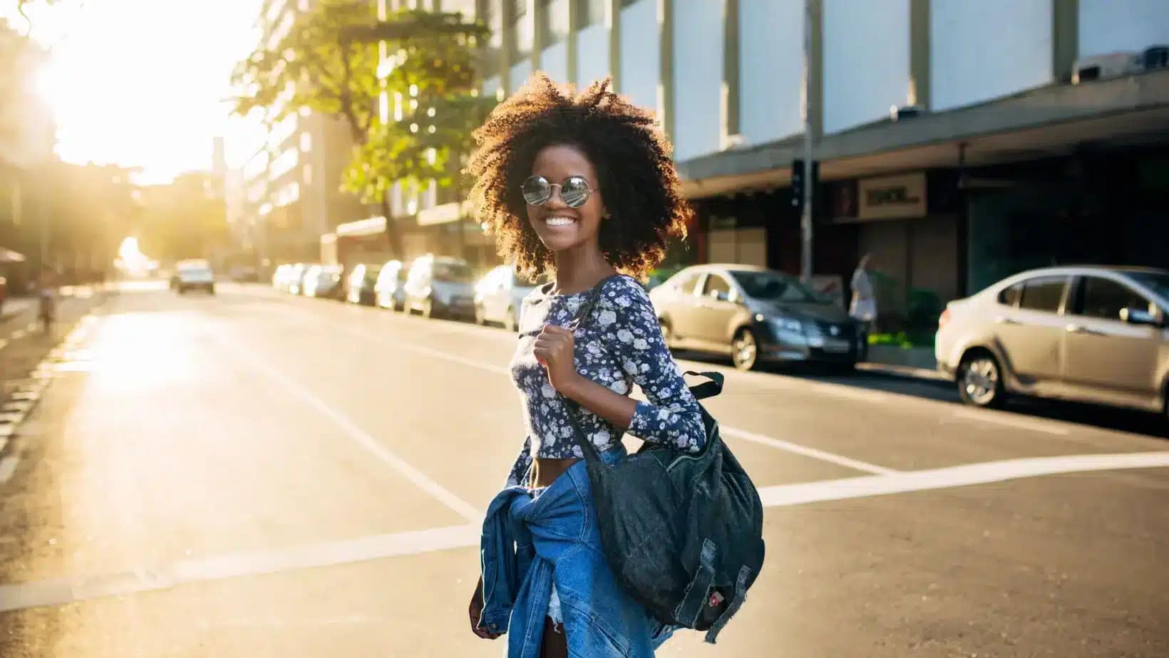 A young woman with a backpack smiling on a sunlit Brazilian city street