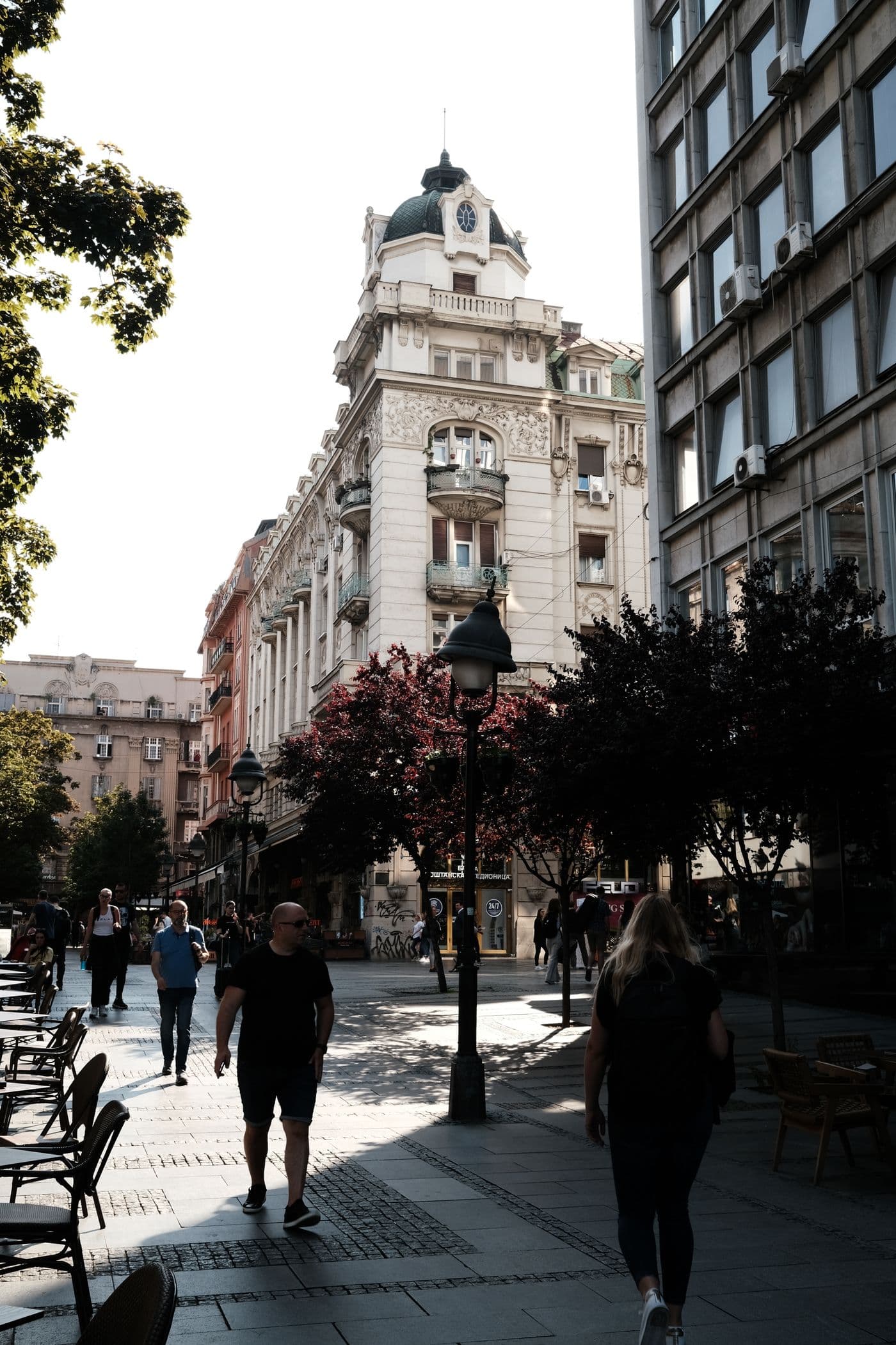 Pedestrian street in central Belgrade with a domed early 1900s apartment building and cafe tables