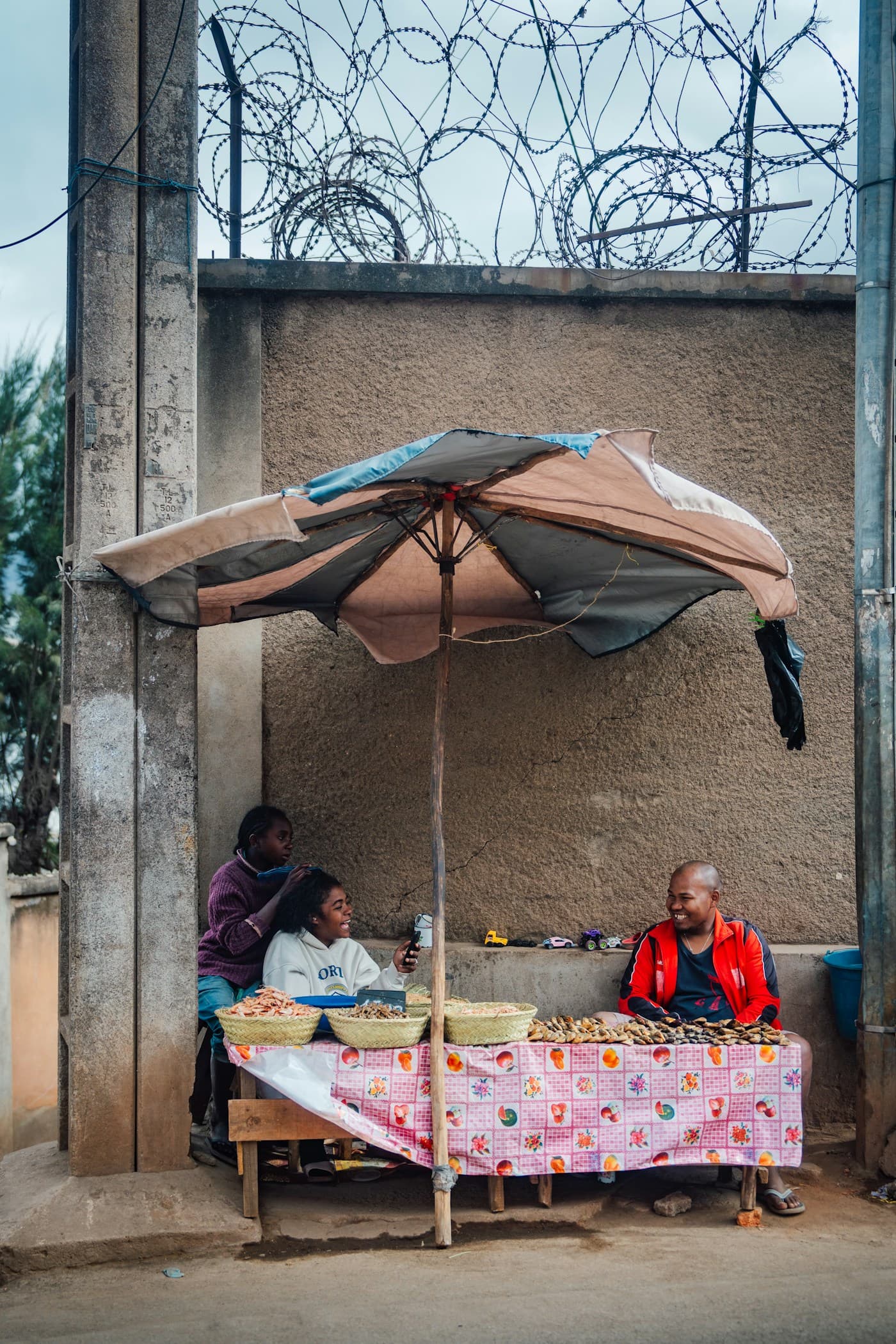 Street vendors selling snacks under a patched umbrella at a roadside stall in Antananarivo, Madagascar