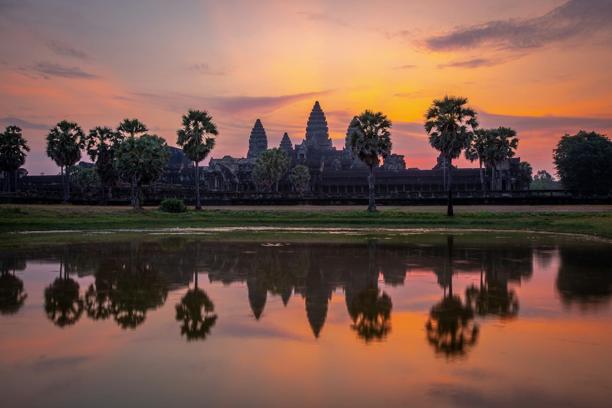 Angkor Wat's towers silhouetted against an orange sunrise and reflected in a pond