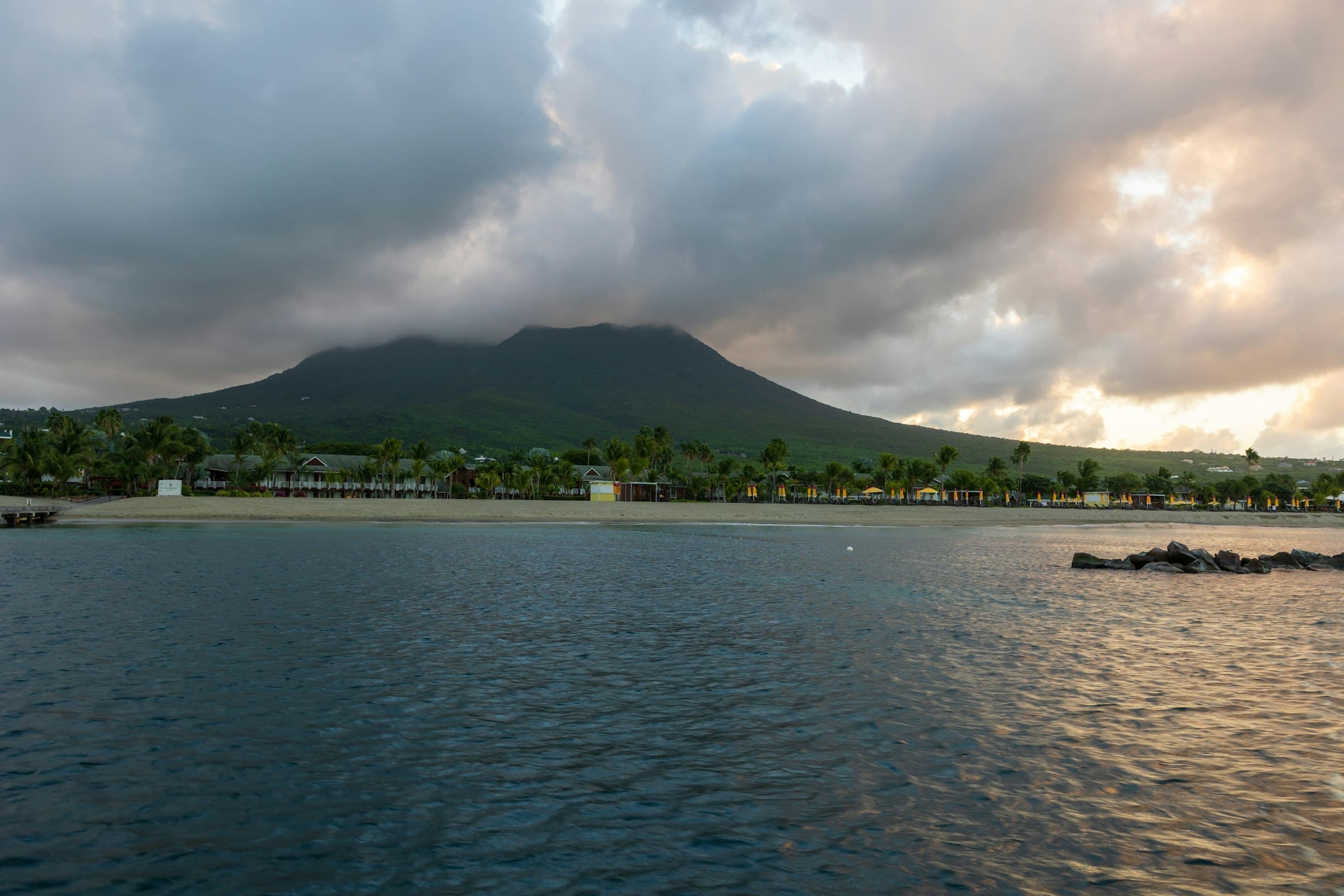 Nevis Peak under cloud above palm trees and a beach on Nevis