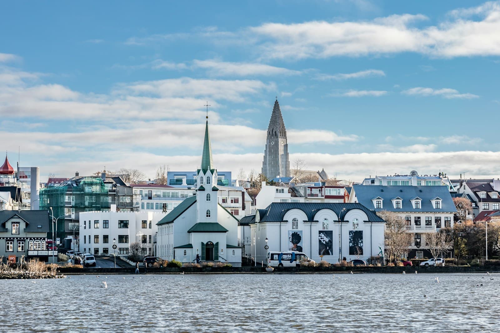 White church and houses along Reykjavík's Tjörnin pond, with Hallgrímskirkja's tower behind