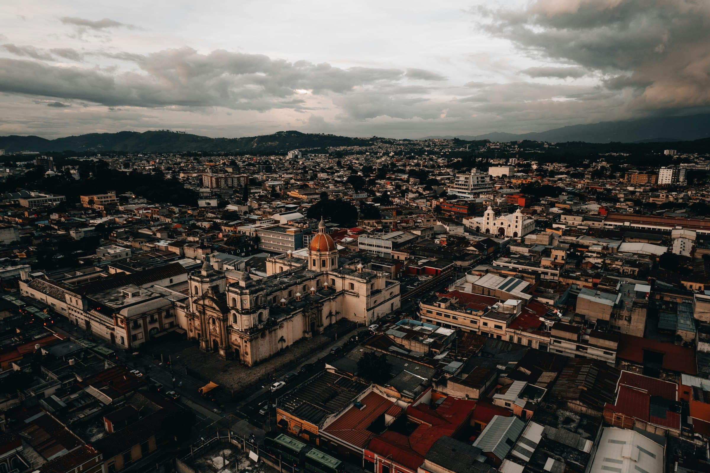 Aerial view of downtown Guatemala City with a domed church and mountains under evening clouds