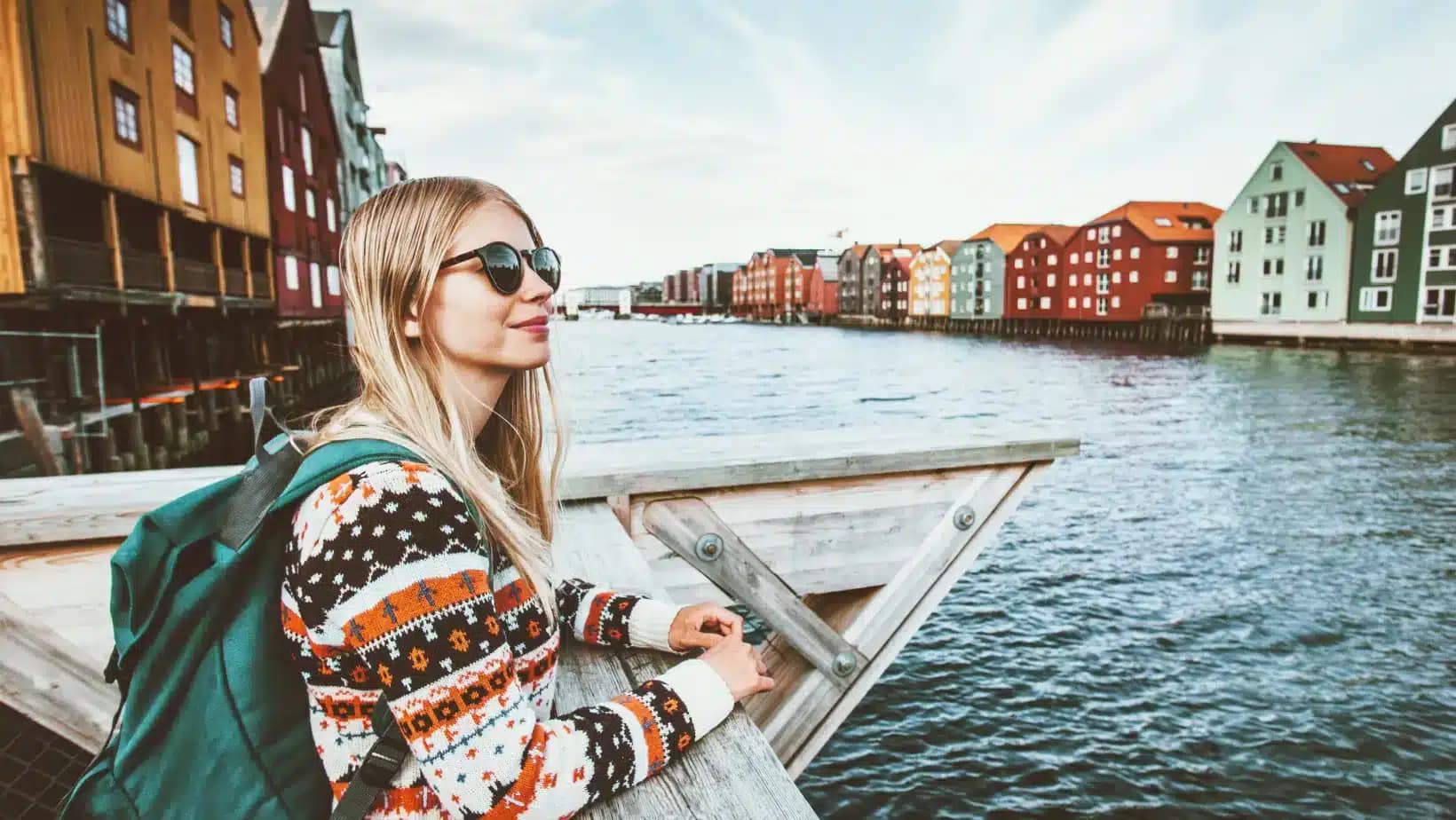A woman with a backpack looks out over the river and colorful wharf houses in Trondheim, Norway