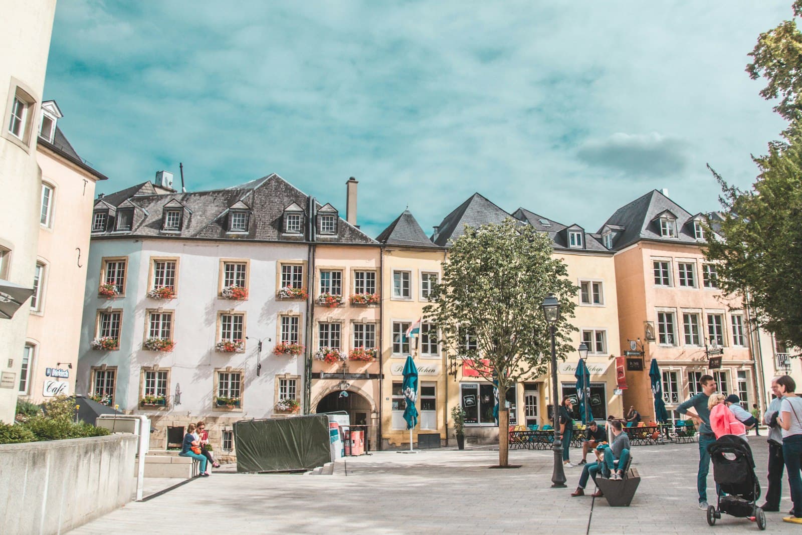 People relaxing on a sunny square lined with pastel townhouses in Luxembourg City