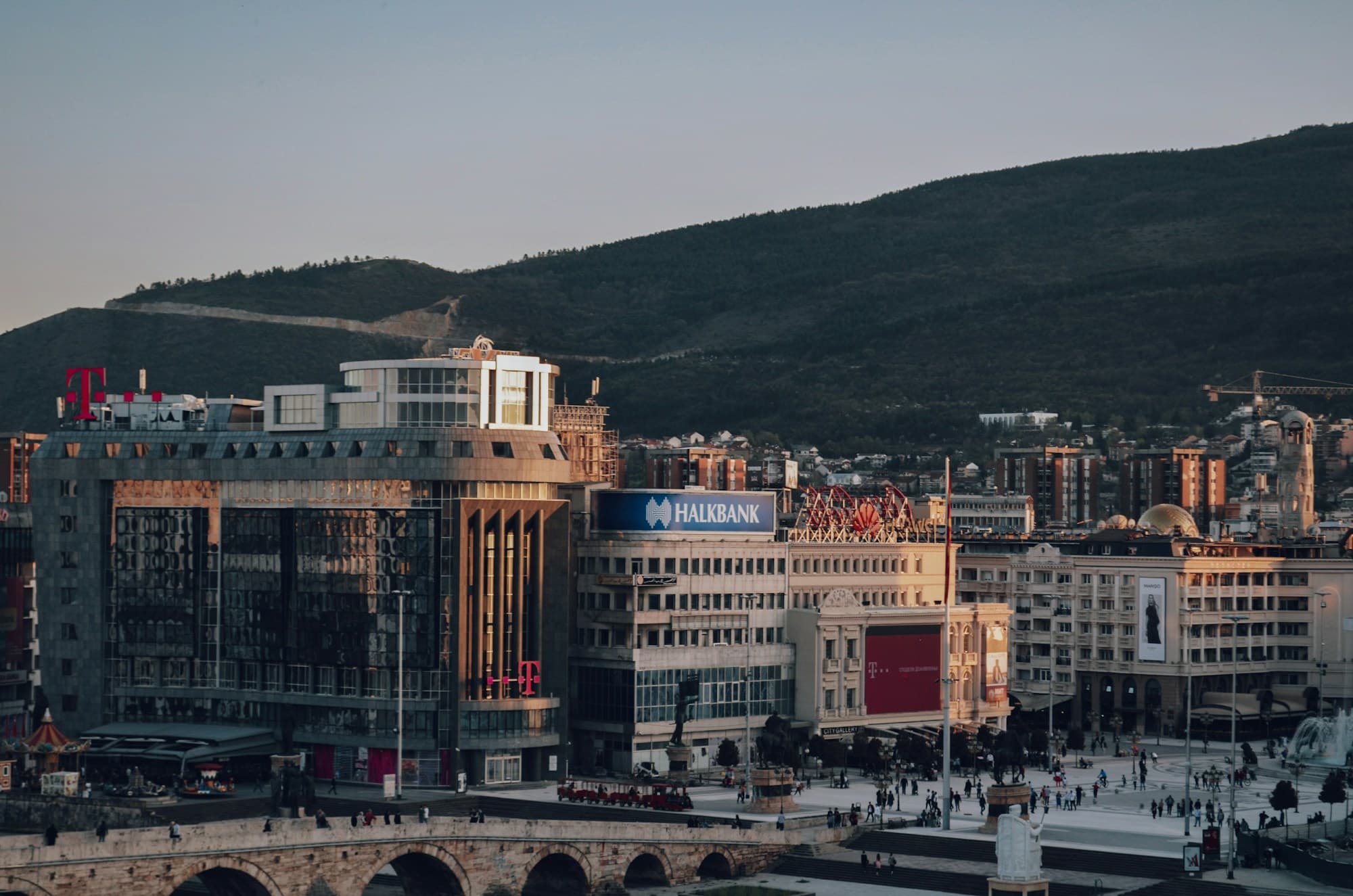 Macedonia Square in Skopje at dusk, with the Stone Bridge and hills behind
