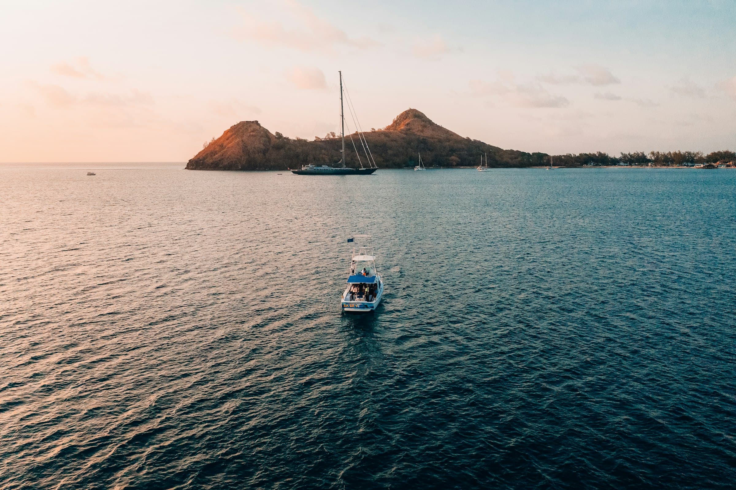 A dive boat on calm water off Pigeon Island in northern Saint Lucia at sunset, with a sailboat anchored nearby