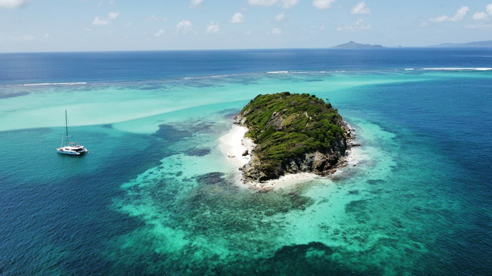 A catamaran anchored beside a small reef-ringed islet in the Grenadines