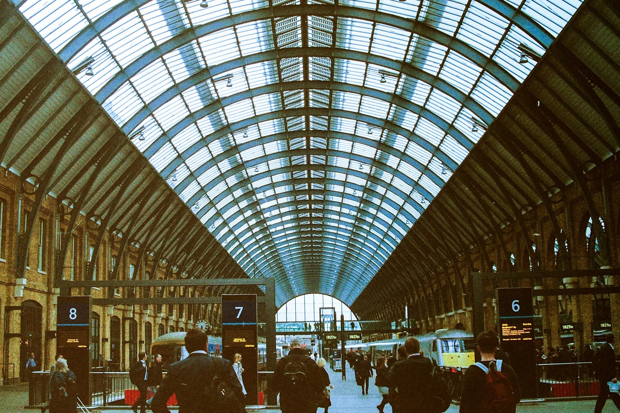 Travelers walking along the platforms under the arched glass roof of King's Cross station in London