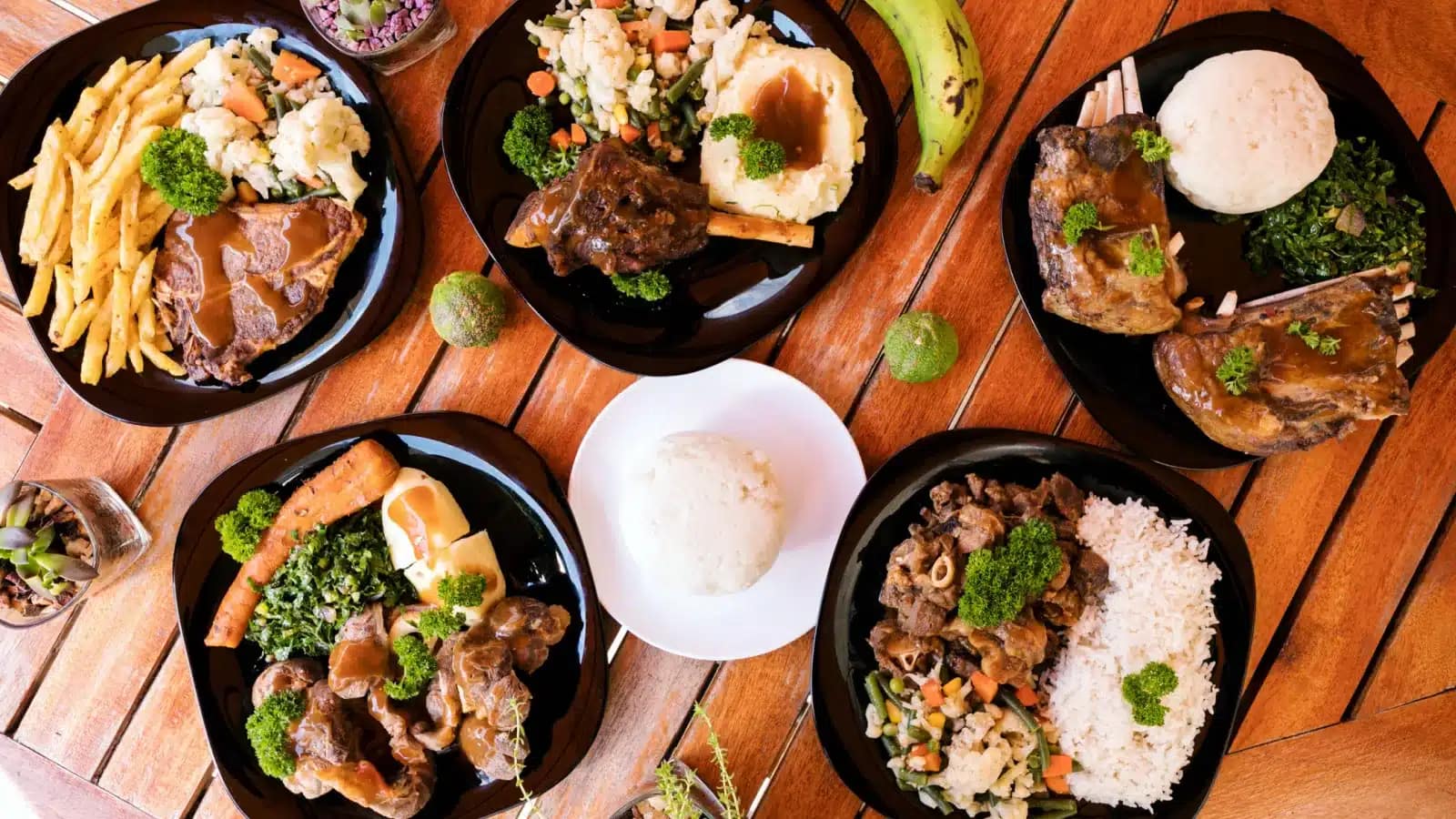 A spread of Kenyan dishes including nyama choma, ugali and greens on a wooden table