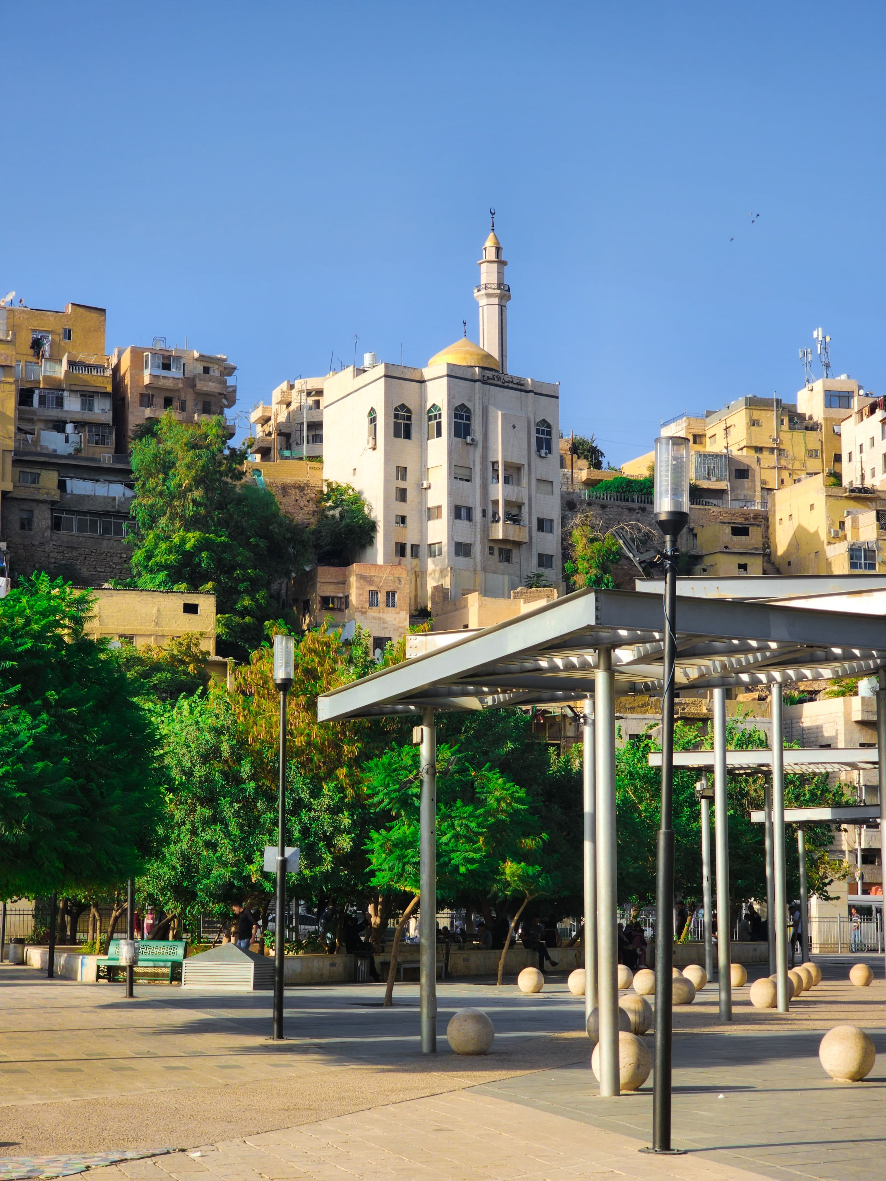 A mosque and hillside homes above a shaded plaza in downtown Amman