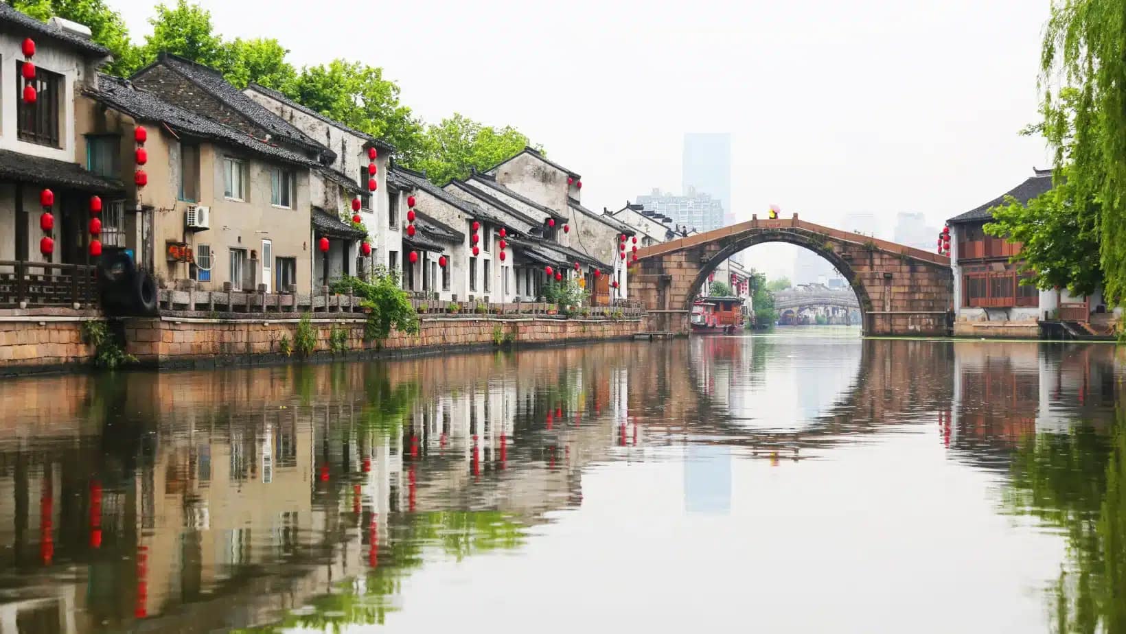 A stone arch bridge over a canal lined with old houses and red lanterns in Wuxi, China