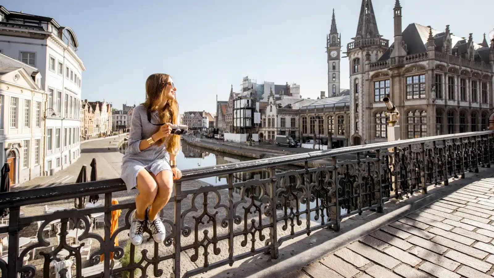 A woman sitting on a bridge railing above the canal in Ghent's historic center