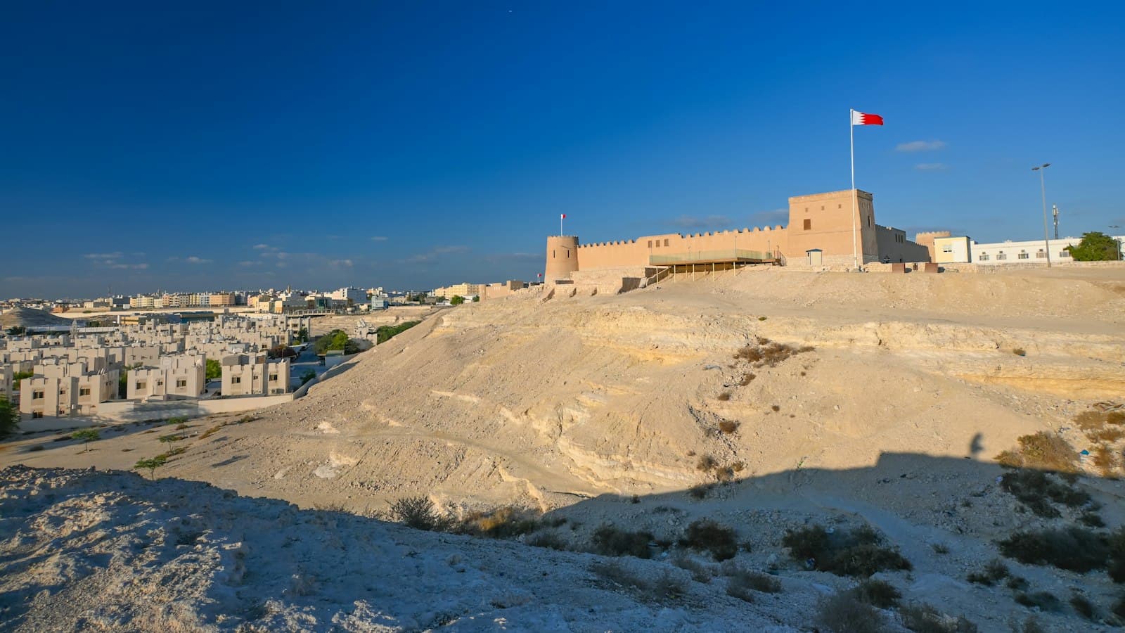 A hilltop fort flying Bahrain's flag above a neighborhood of low sand-colored homes