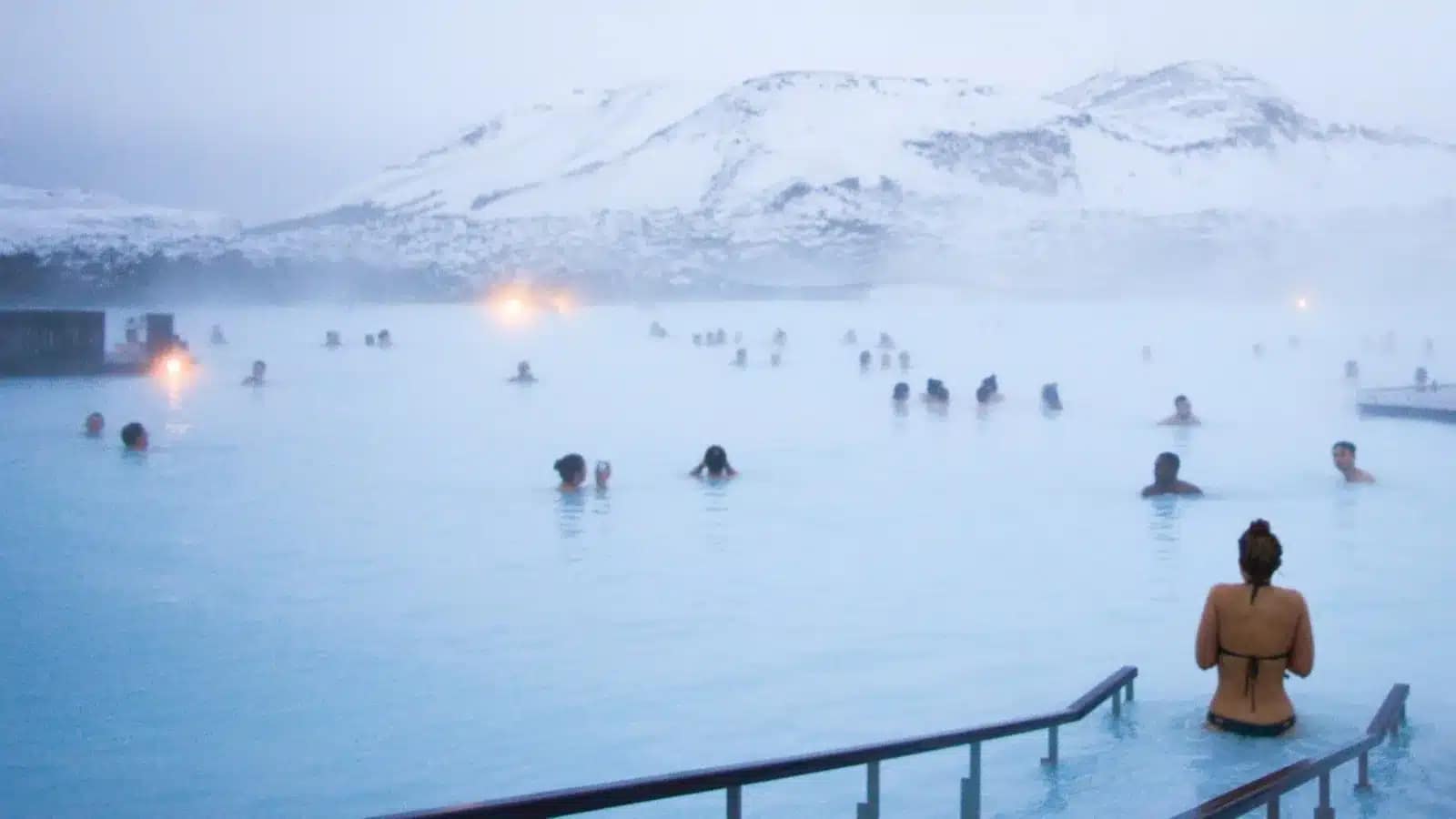 Bathers in a steaming geothermal lagoon below snowy hills in Iceland