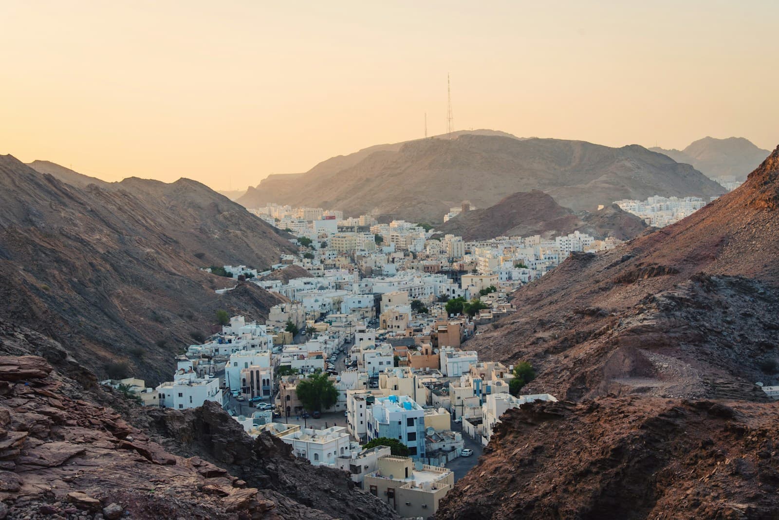 White houses filling a valley between rocky hills in Muscat, Oman, at sunset