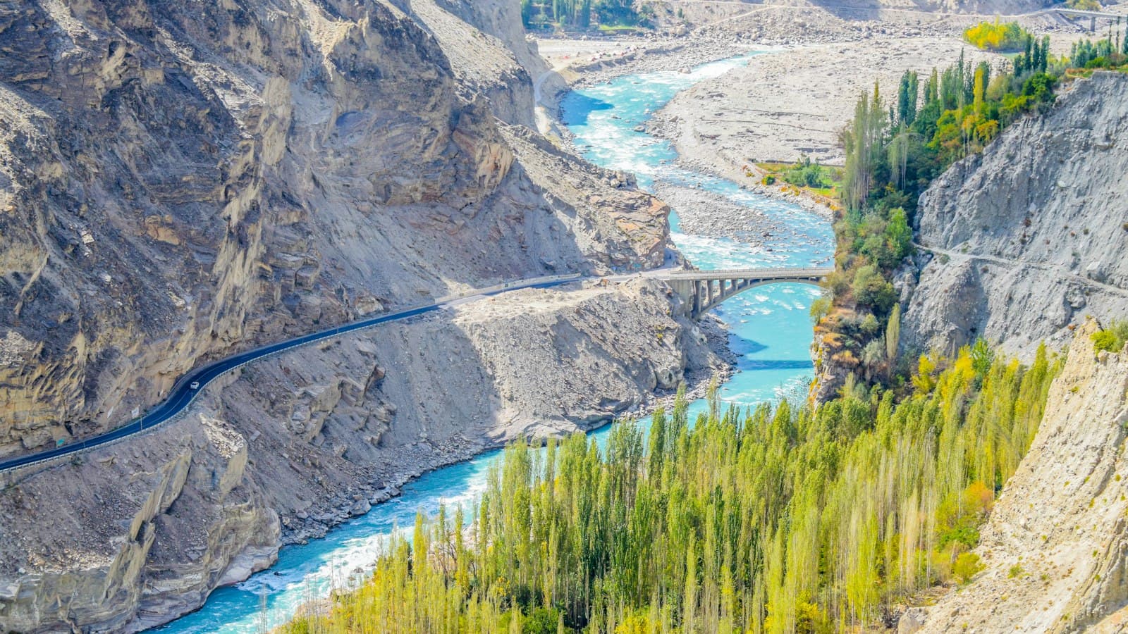 A turquoise river, a highway bridge and poplar trees in a mountain valley in northern Pakistan
