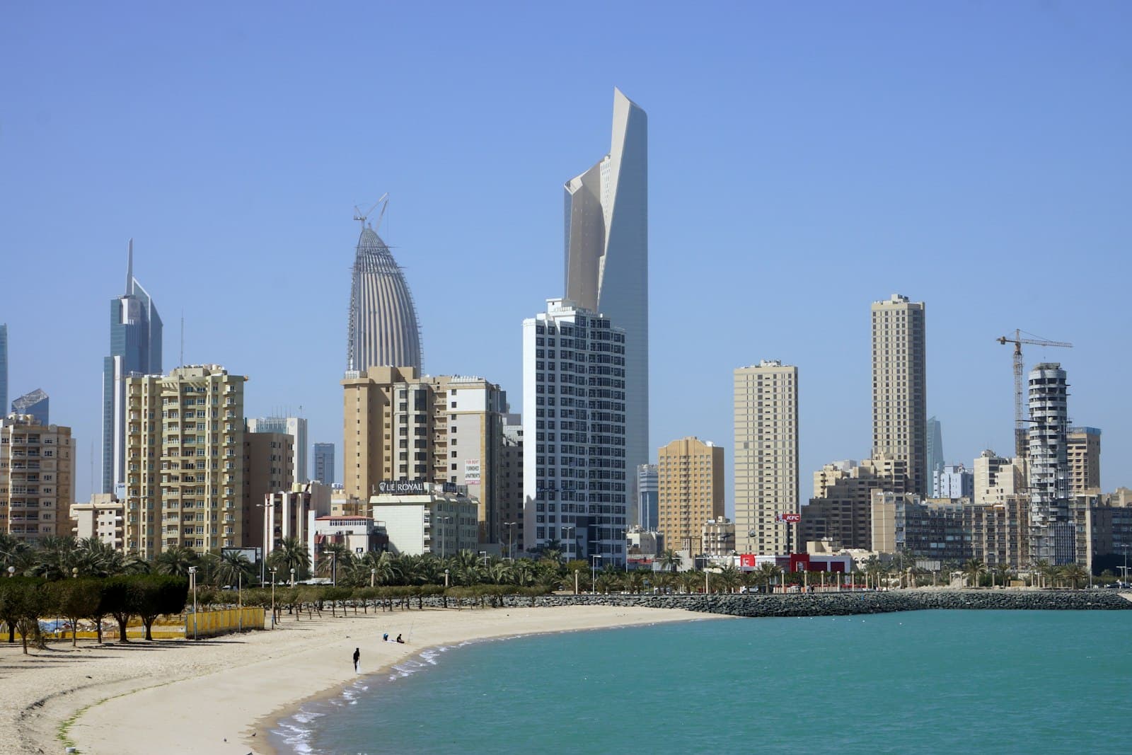 Kuwait City towers rising behind a curved public beach on the Gulf