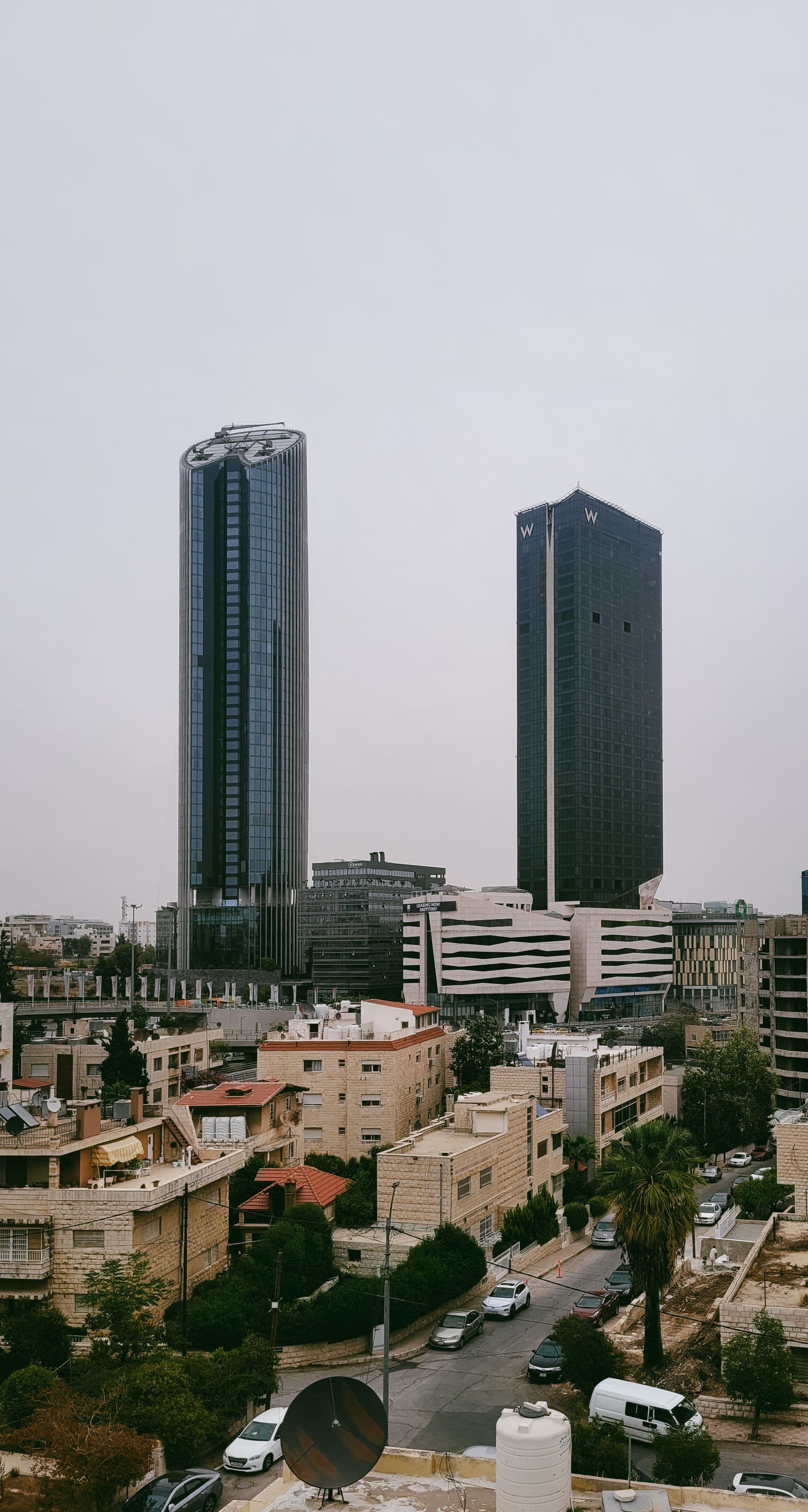 Glass office towers rising over stone apartment buildings in Amman's Abdali district