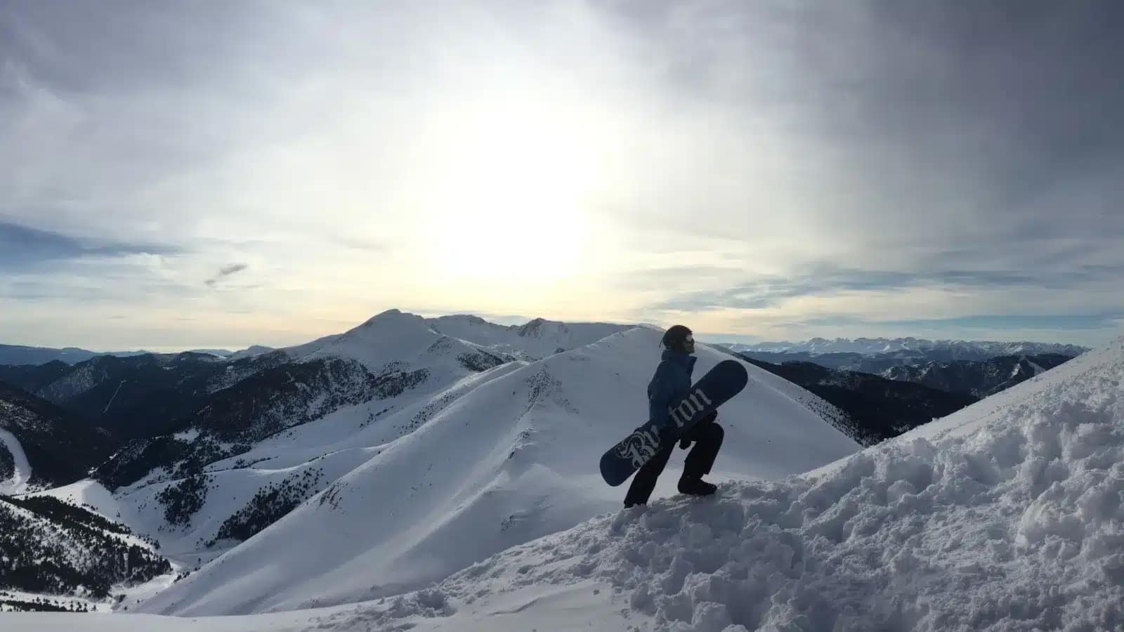A snowboarder standing on a snowy ridge above the Andorran Pyrenees