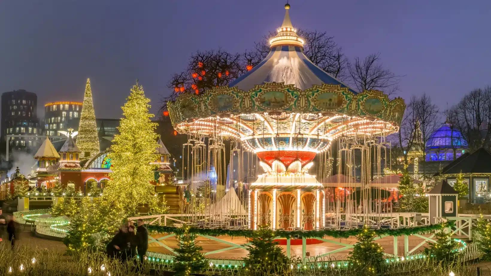 A lit carousel and Christmas trees in Tivoli Gardens, Copenhagen, on a winter evening