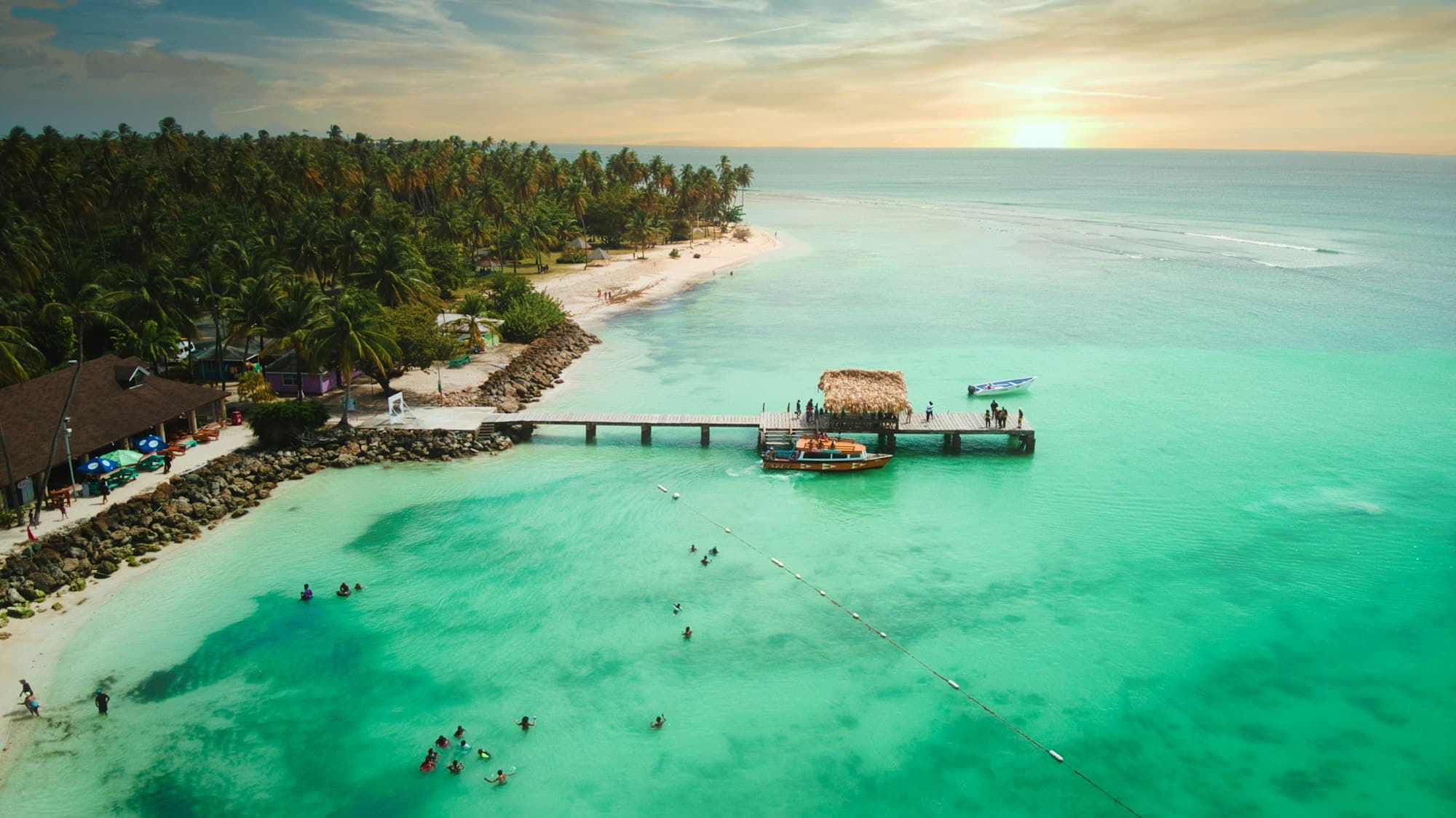 Aerial view of a wooden pier and turquoise water off a palm-lined beach in Tobago